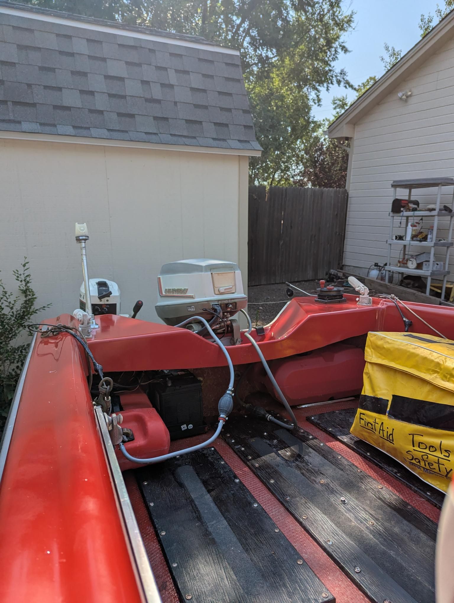 A red 1972 14-foot Swiss Craft runabout with an outboard motor, parked beside a shed.