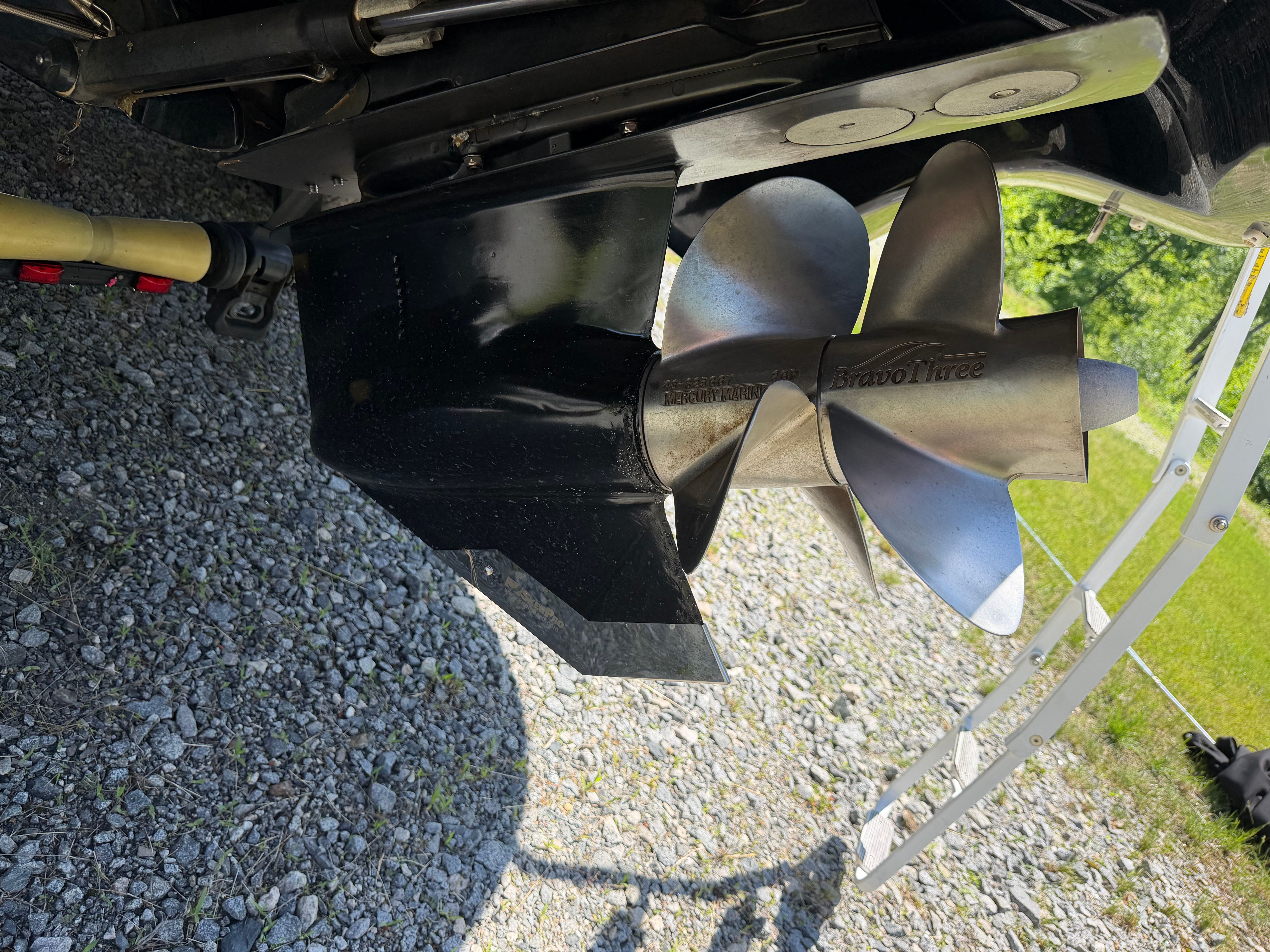 Close-up of a boat propeller on a gravel surface.