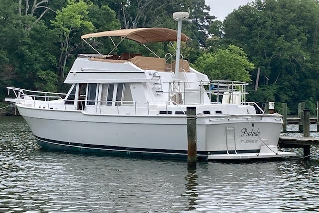 2000 Mainship 430 Trawler docked on a serene waterway with lush greenery.
