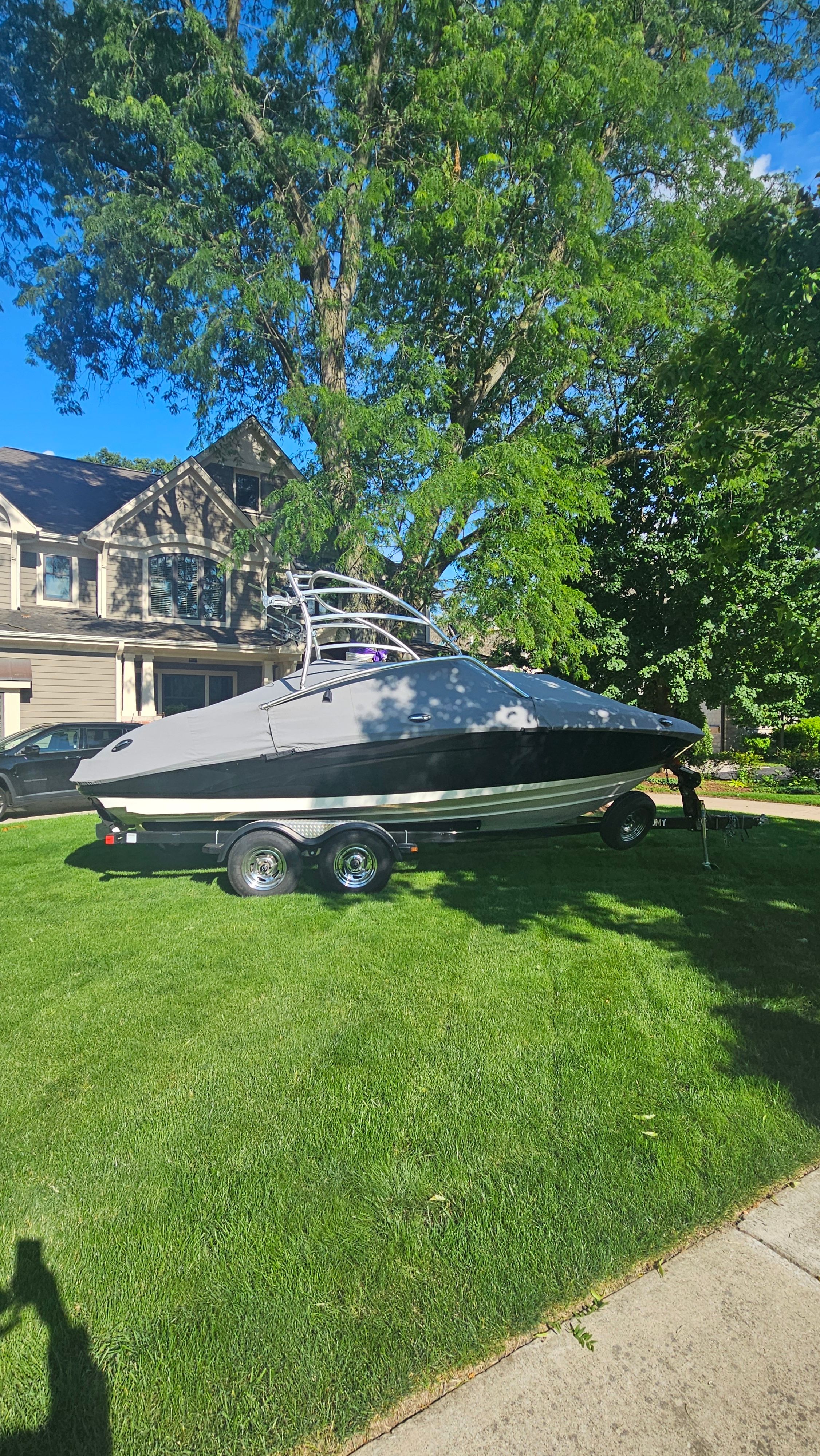 A 2010 Yamaha AR210 boat on a trailer in a house's front yard.
