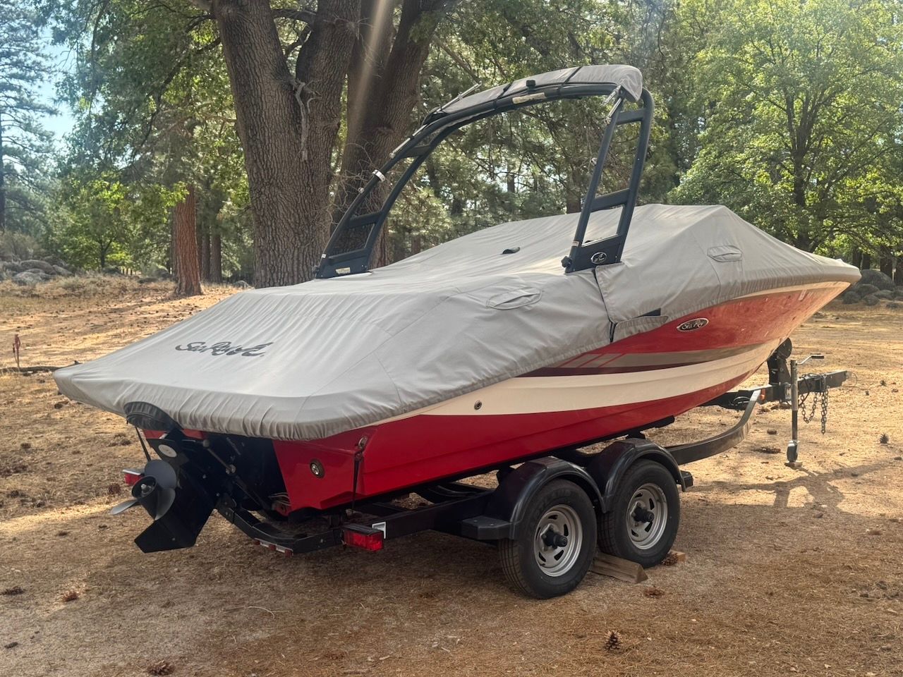 A red 2016 Sea Ray SPX 190 Outboard boat on a trailer in a wooded area.