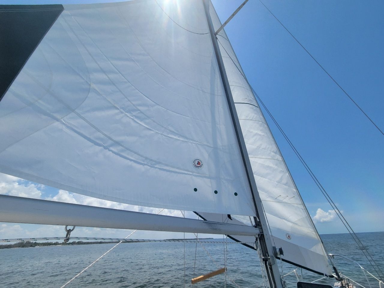 Sailboat with white sails on open water under a blue sky.