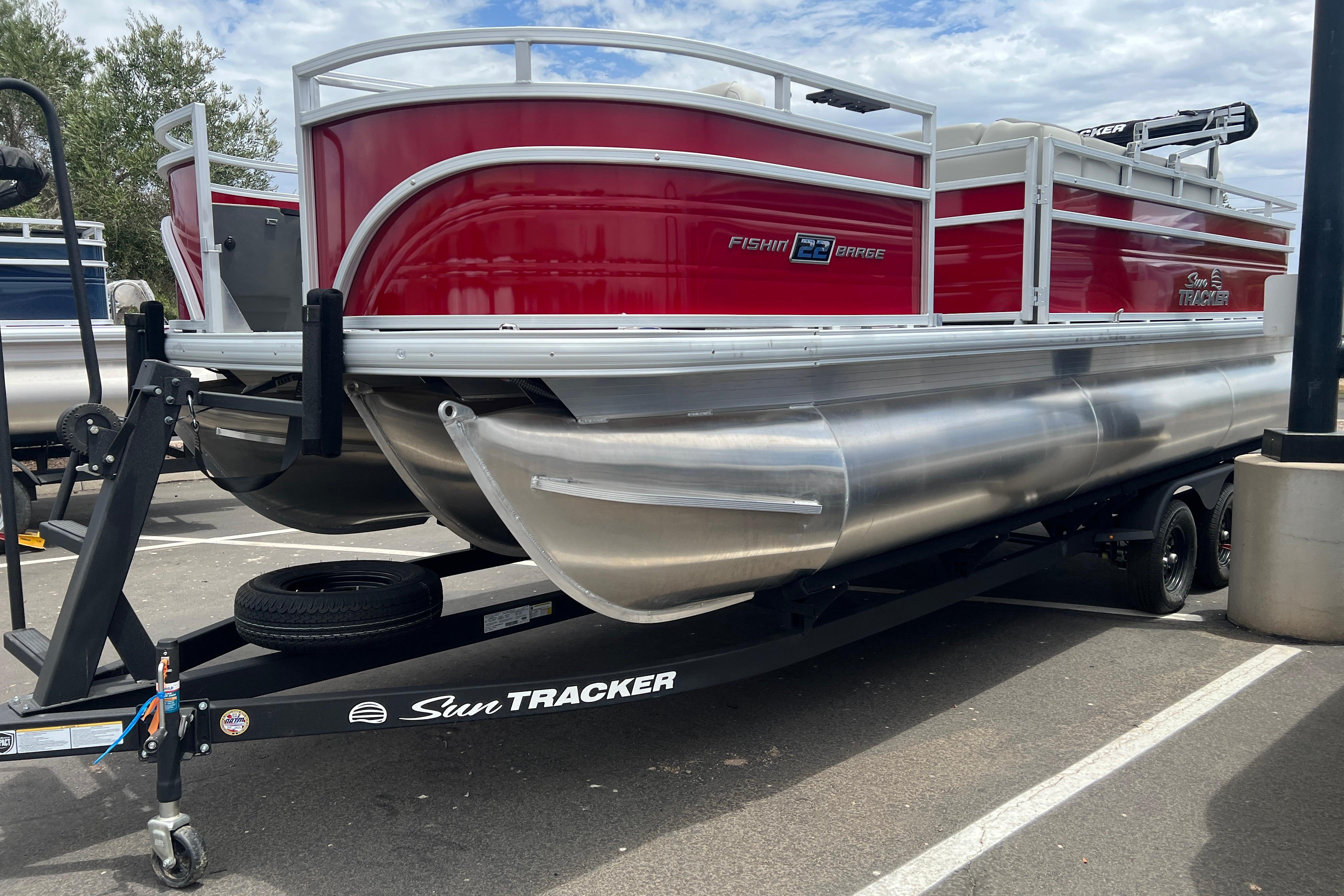 2026 Sun Tracker Fishin' Barge 22 XP3 pontoon boat on trailer, red and silver design.