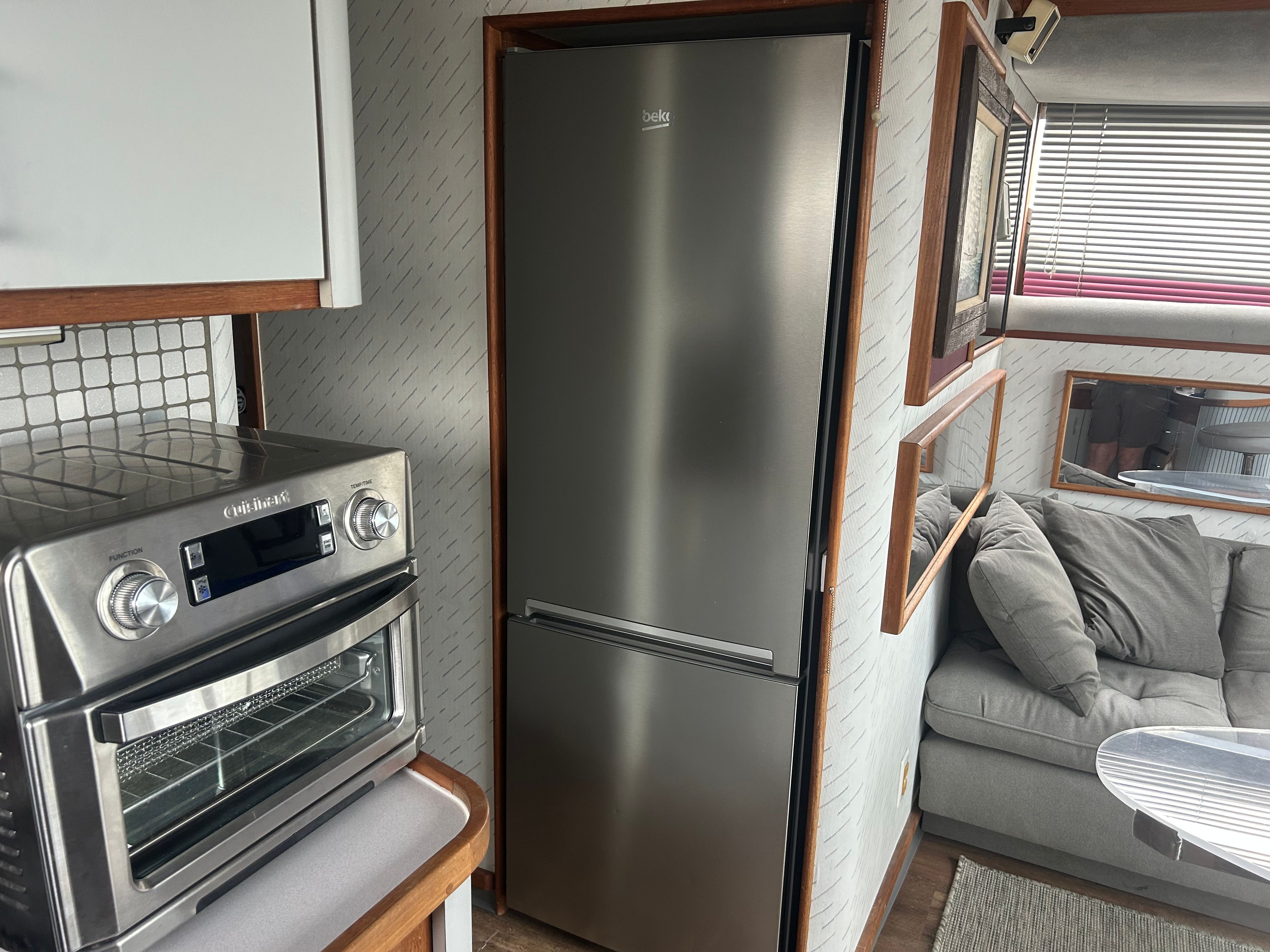 Interior of a yacht with a fridge, oven, and gray sofa.