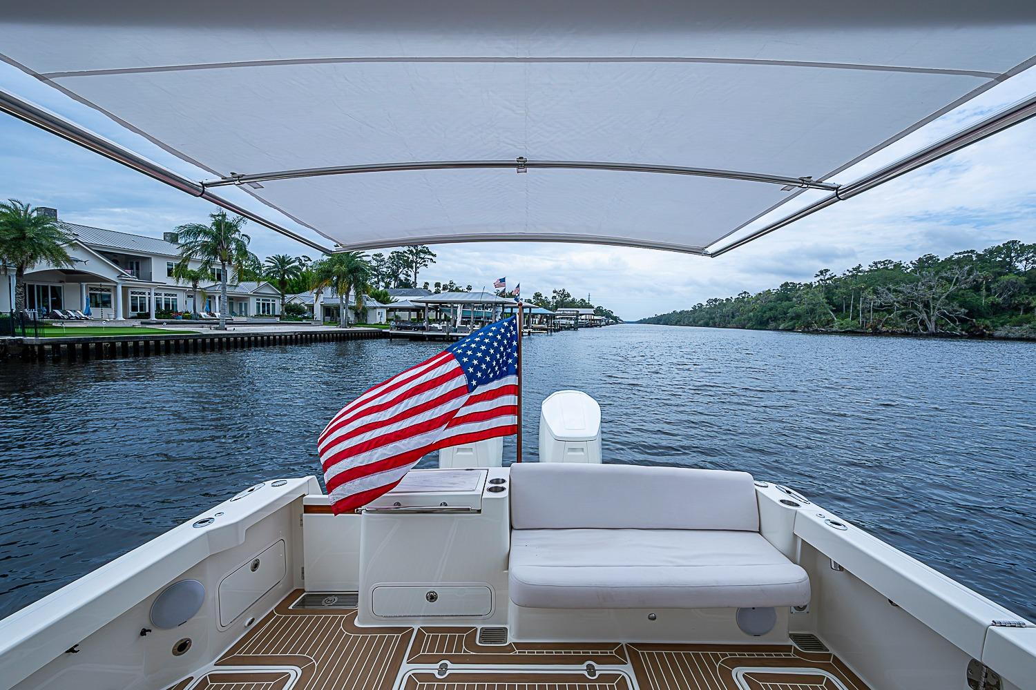2023 Hinckley Sport Boat 40 X cruising on a scenic river with American flag.
