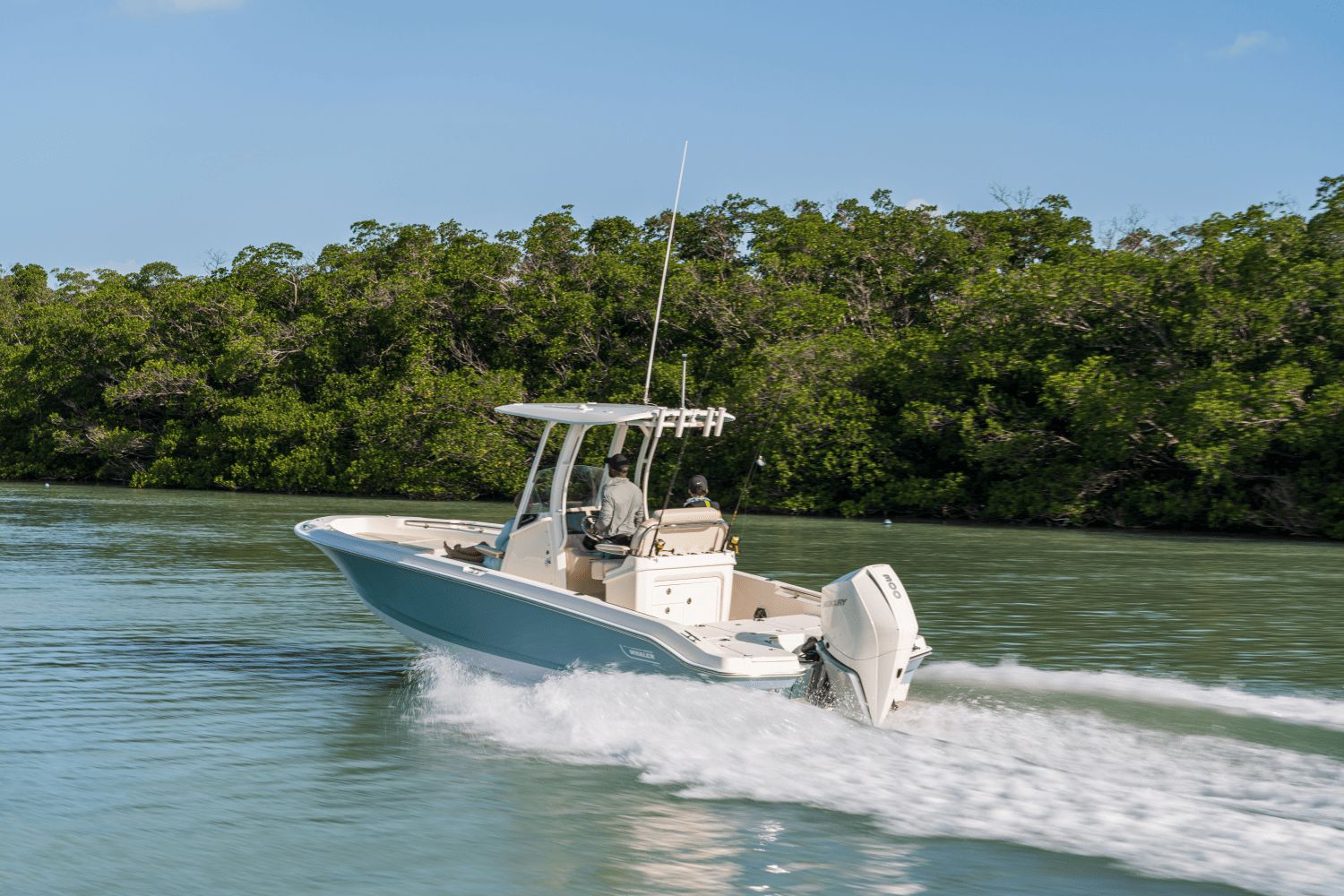 A Boston Whaler 25DA boat speeds through calm water, surrounded by lush greenery.