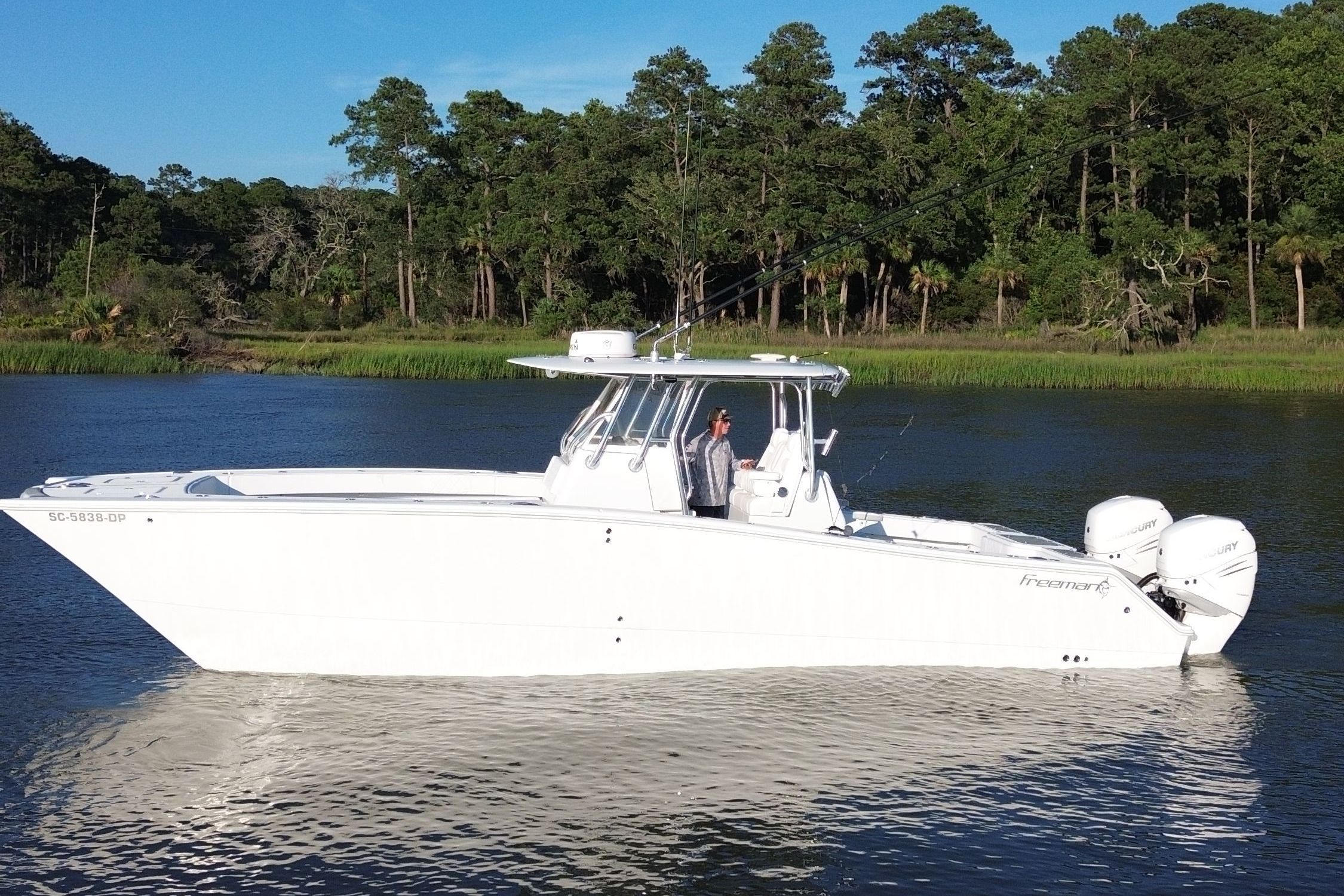 A white boat floating on calm water, surrounded by trees.
