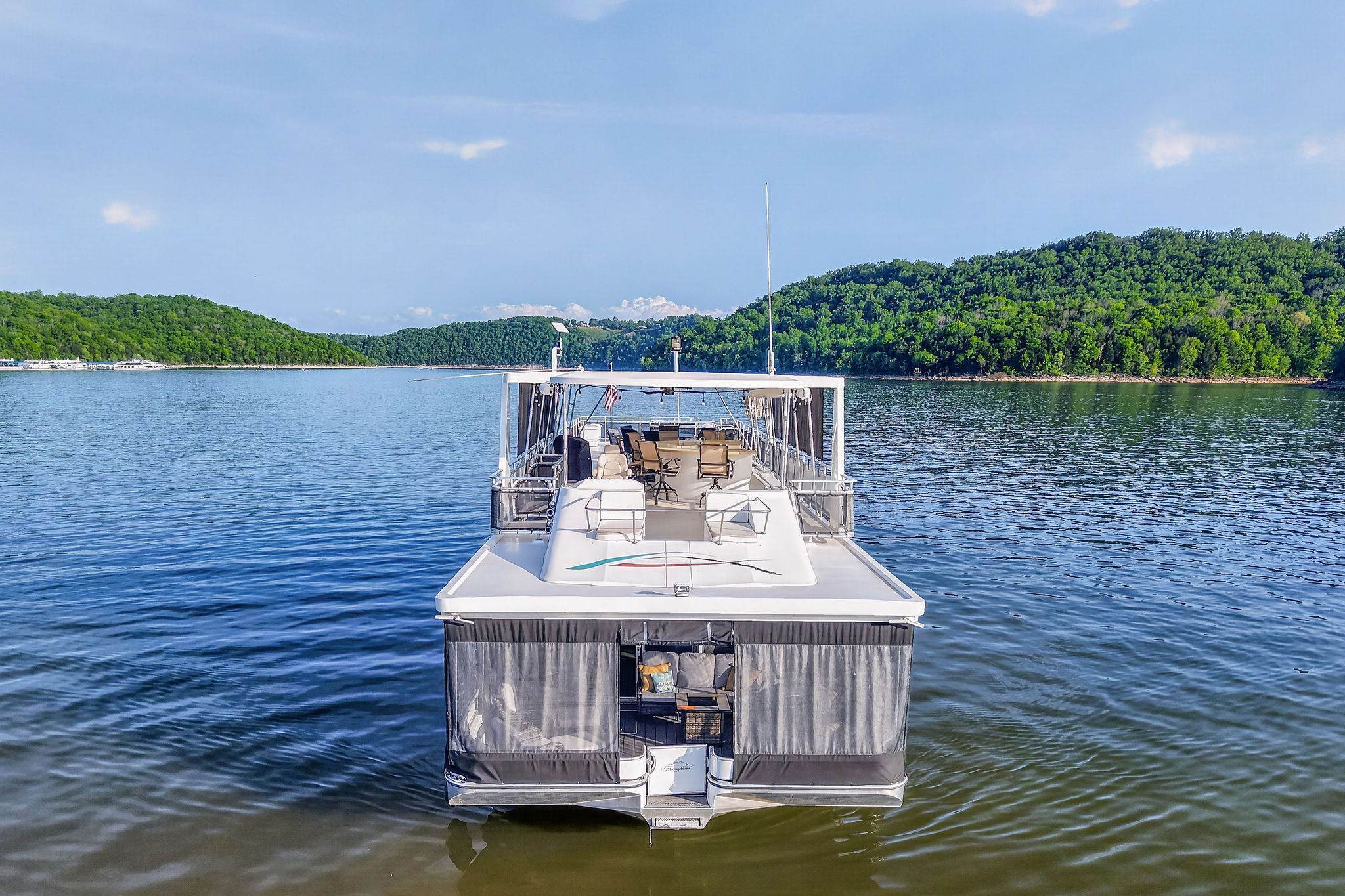 Houseboat on serene lake with wooded shores, model Throughbred 2010.