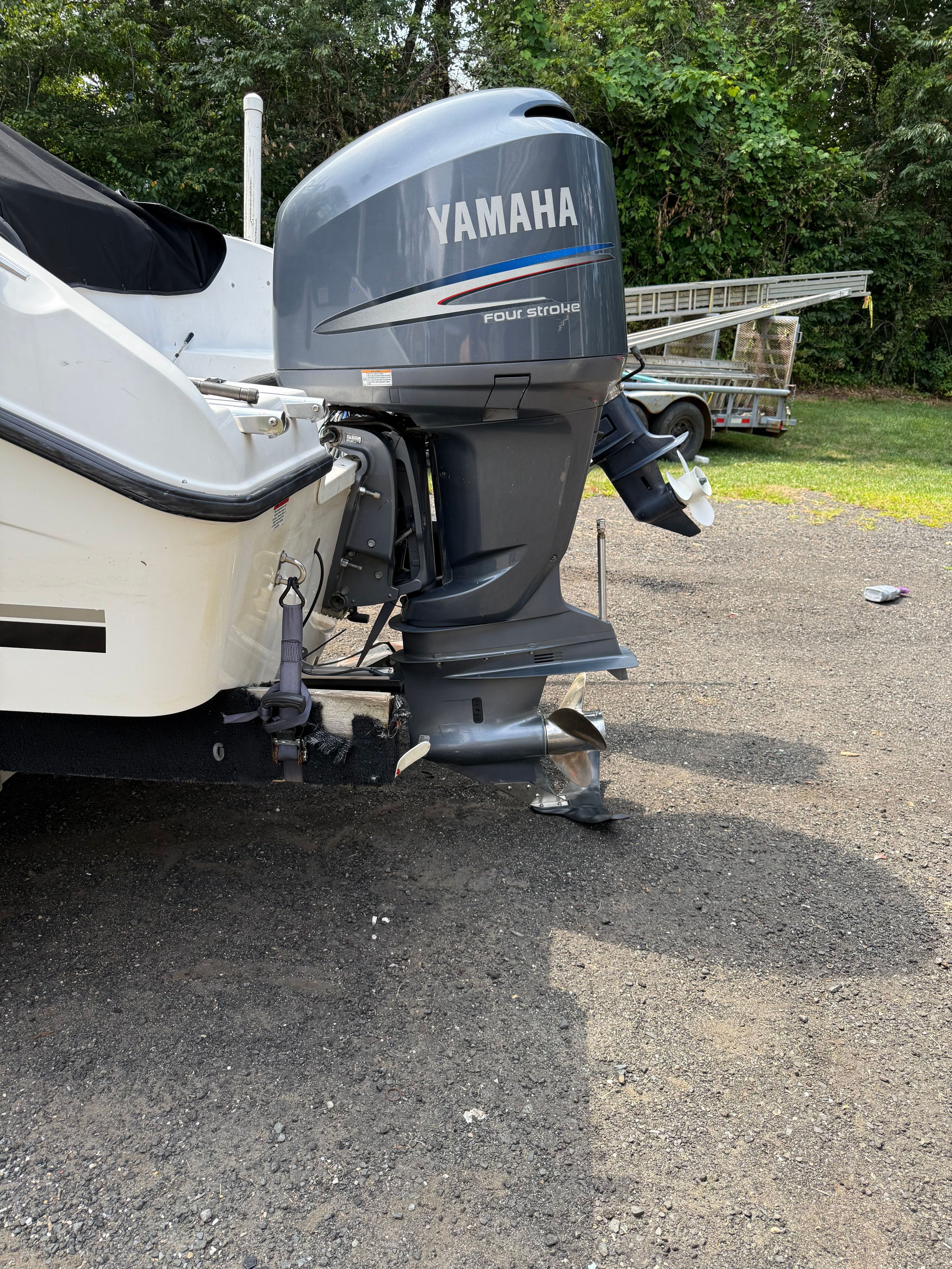 A Yamaha four-stroke engine is mounted on the stern of a white boat on a gravel lot.