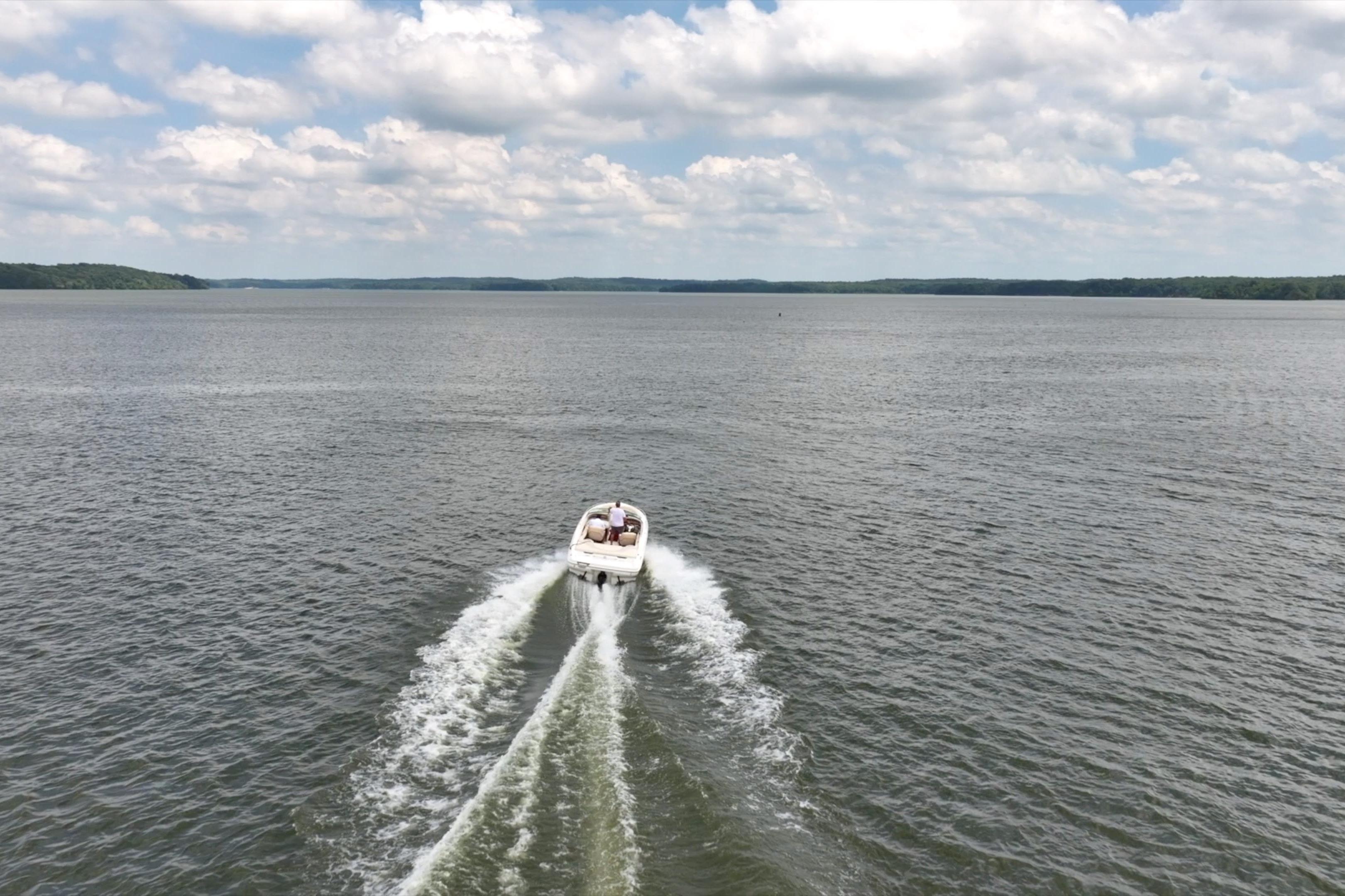 1997 Sea Ray 230 Signature boat cruising on a vast lake under a cloudy sky.