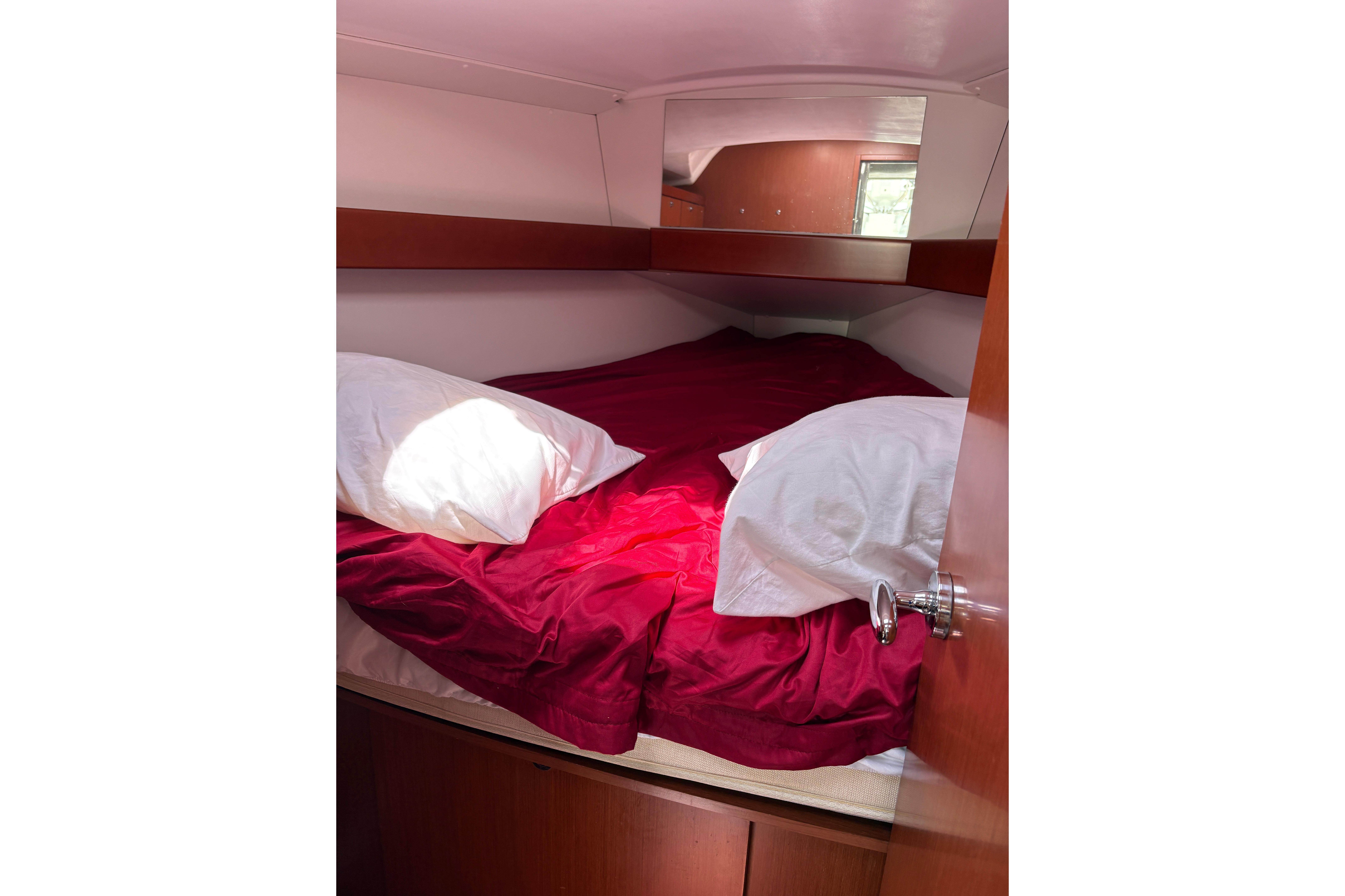 Cozy cabin interior of 2015 Beneteau Oceanis 34 with red bedding and pillows.
