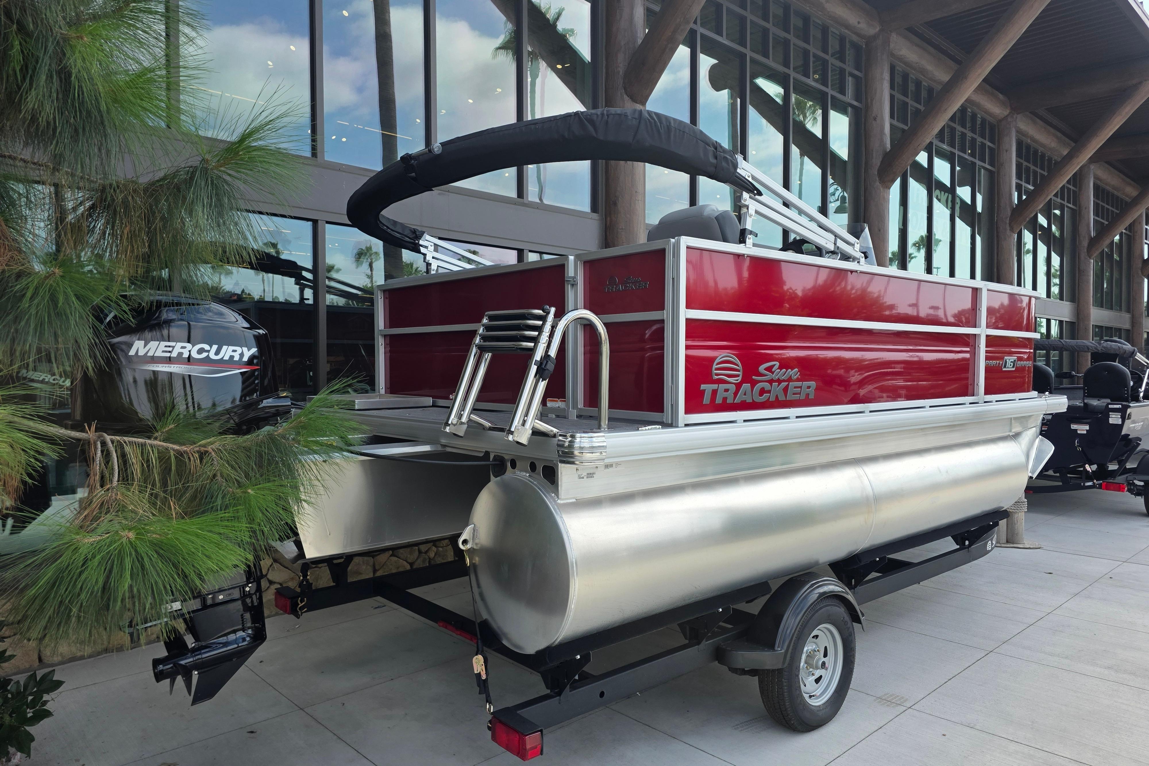 2026 Sun Tracker Party Barge 16 DLX pontoon boat with Mercury engine, parked outdoors.