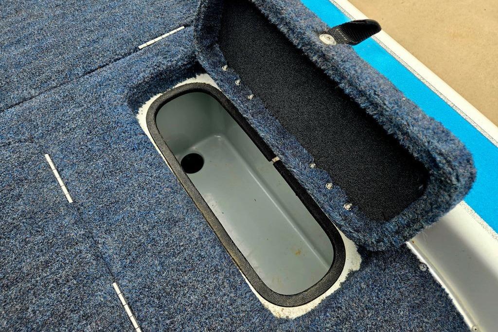 Open storage compartment on 1996 Champion 181 SX boat with blue carpet interior.
