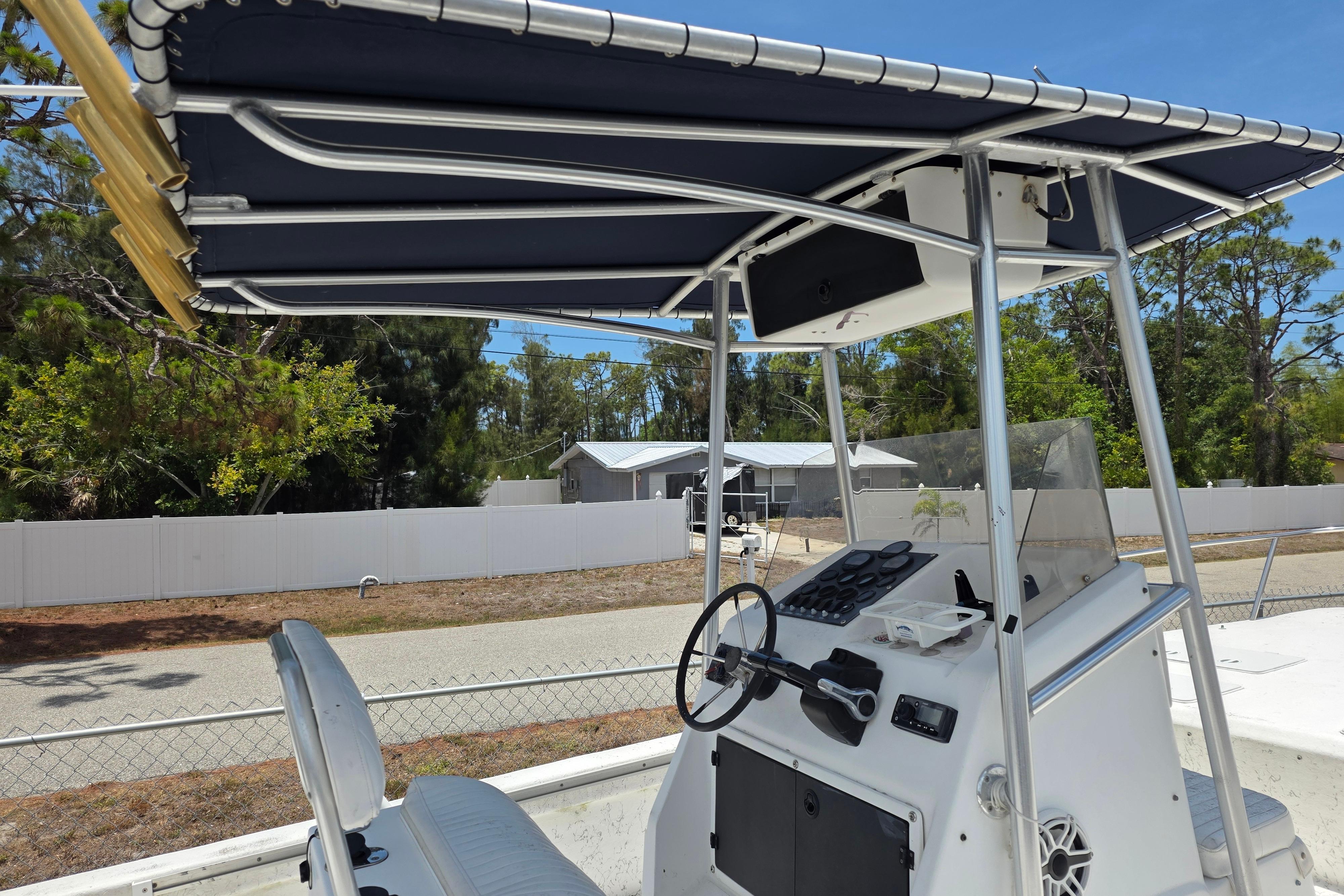 1999 Twin Vee Awesome 22 boat cockpit with steering wheel and canopy, parked outdoors.