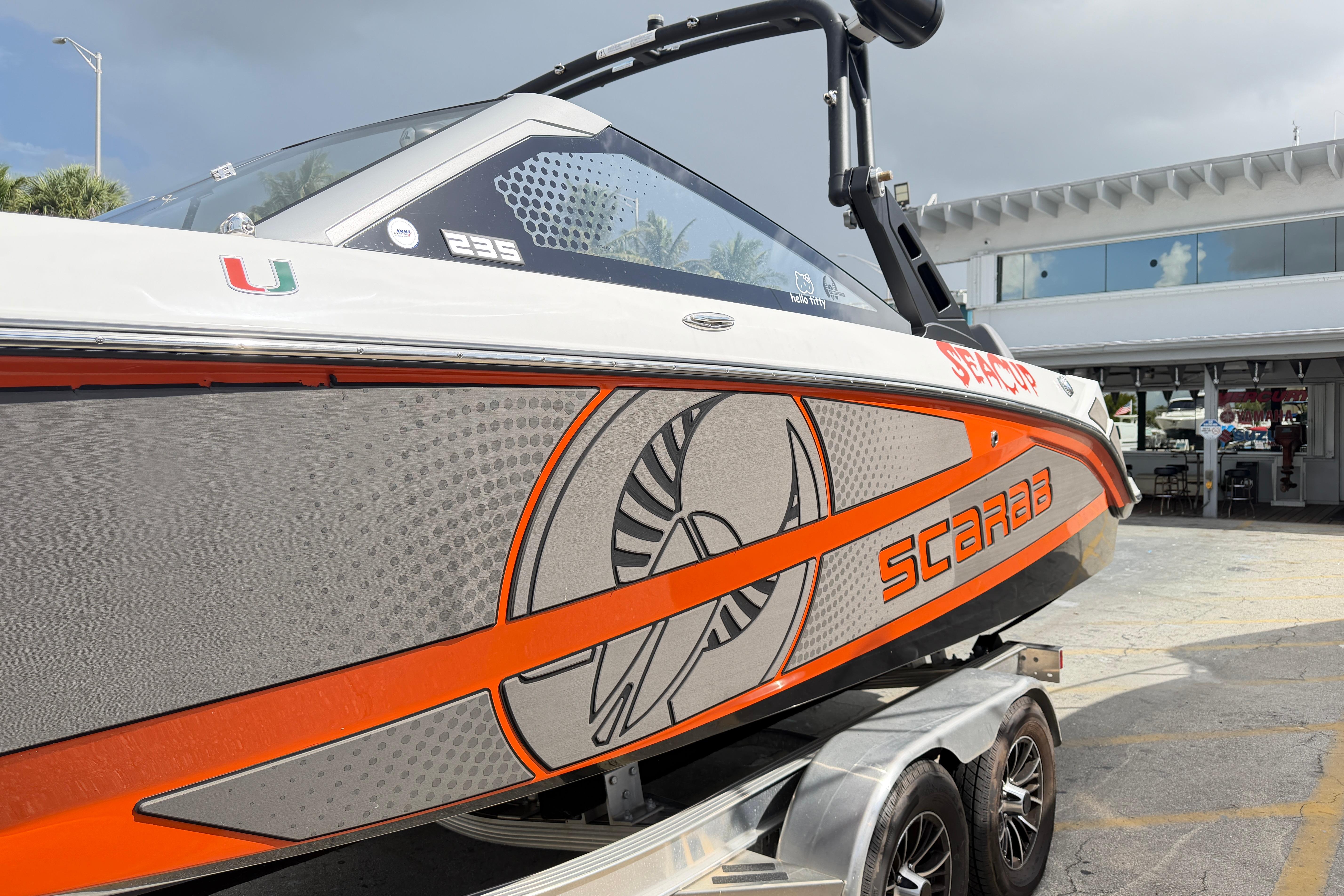 2026 Scarab 235 LX boat with vibrant orange and gray design on a trailer.