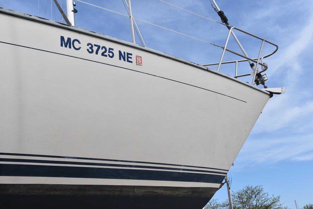 Bow of a white sailboat with blue stripes, on a trailer on land.