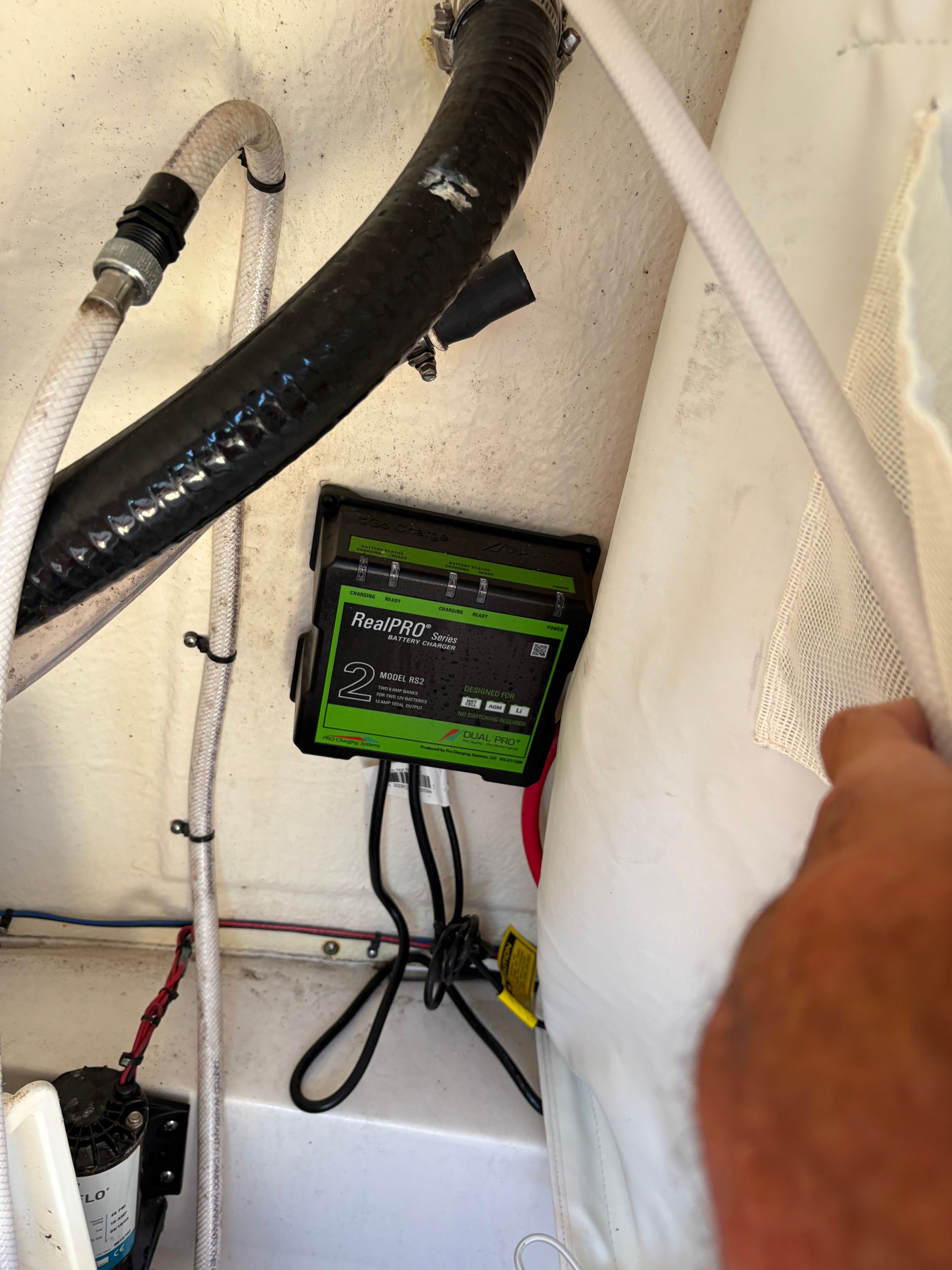 A charger is installed in a boat, surrounded by cables and hoses.