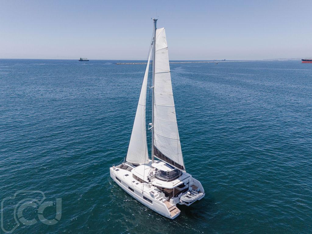 2021 Lagoon 46 catamaran sailing on open sea under clear blue sky.