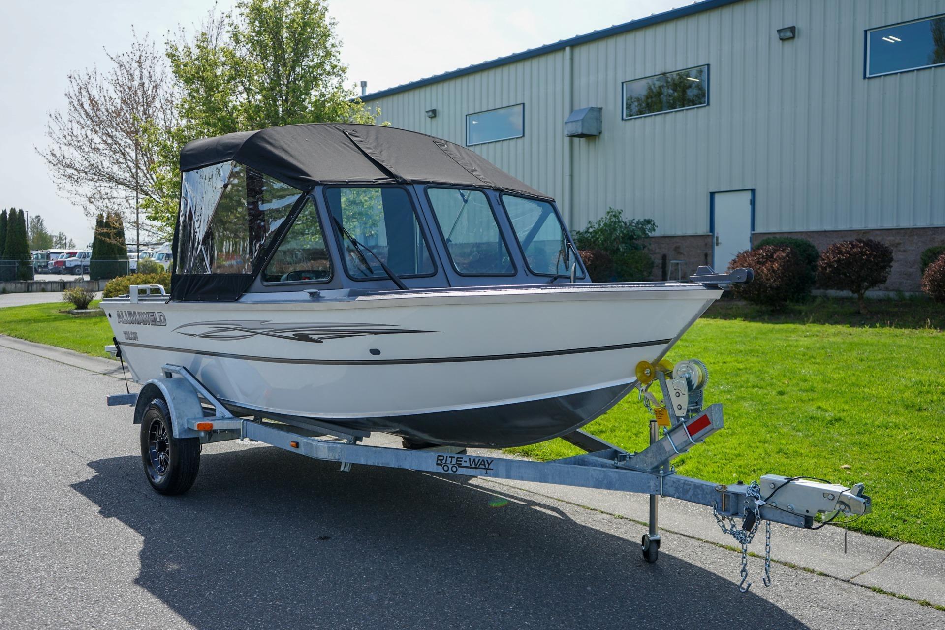 2026 Alumaweld Talon 18 boat on trailer, parked outdoors near industrial building.
