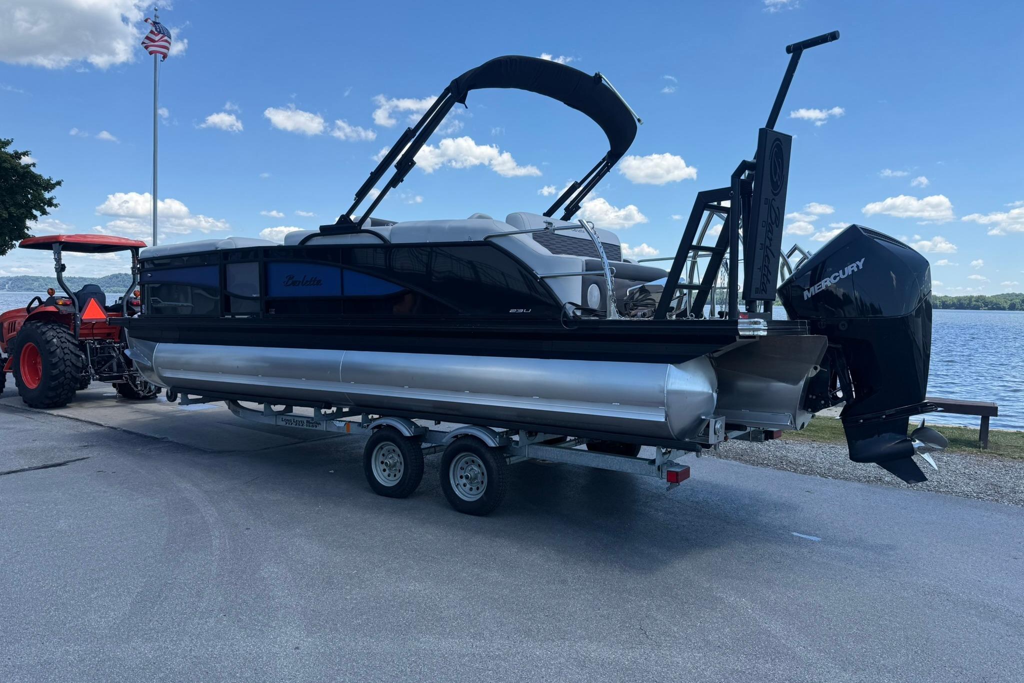 2023 Barletta Corsa 23U pontoon boat on trailer by a lake, with a Mercury engine.
