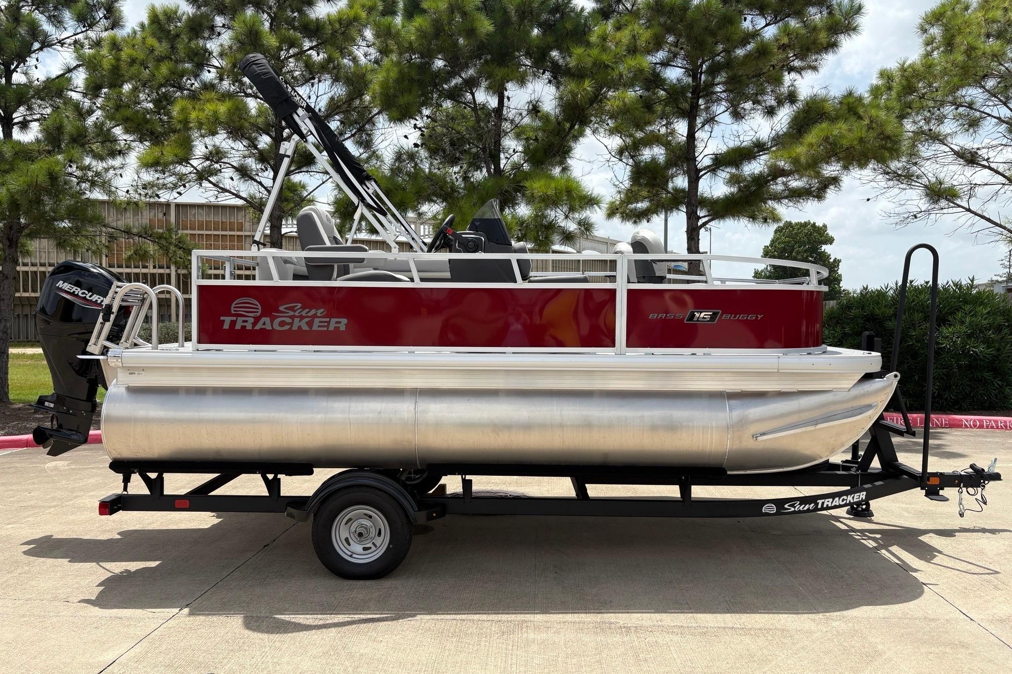 2026 Sun Tracker Bass Buggy 16 XL Select pontoon boat on trailer, parked outdoors.