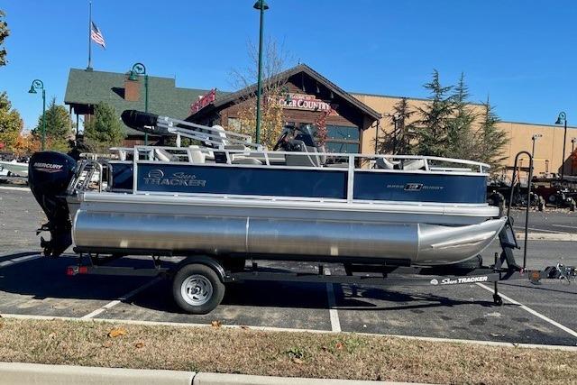 2026 Sun Tracker Bass Buggy 18 DLX pontoon boat on trailer in parking lot.