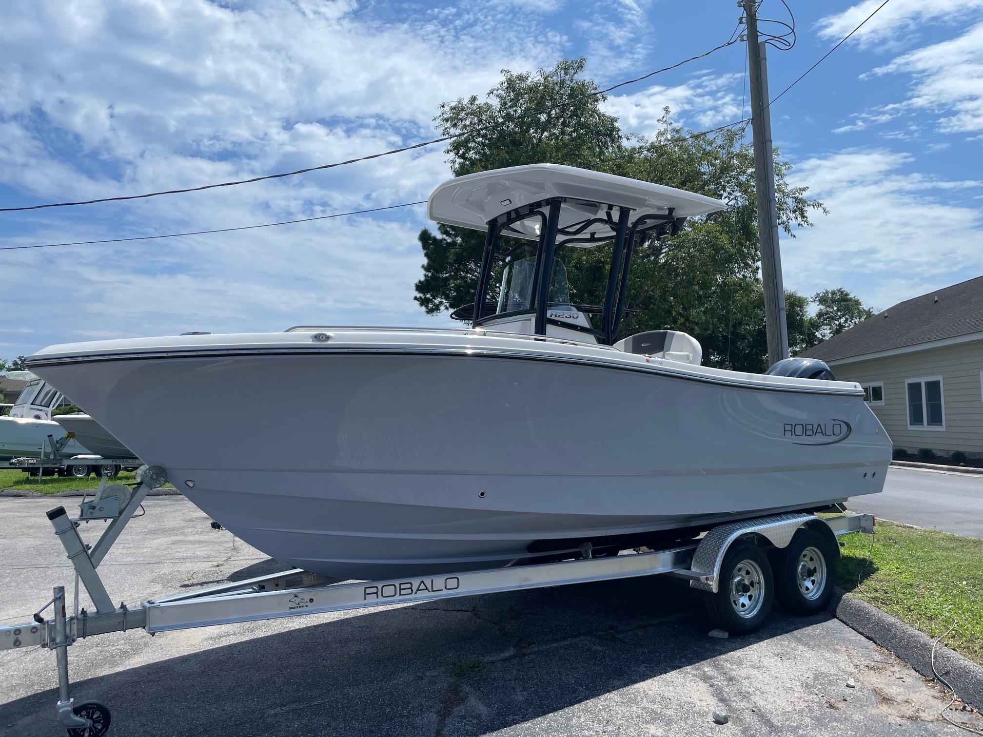 2025 Robalo R230 Center Console boat on trailer, parked outdoors under a blue sky.