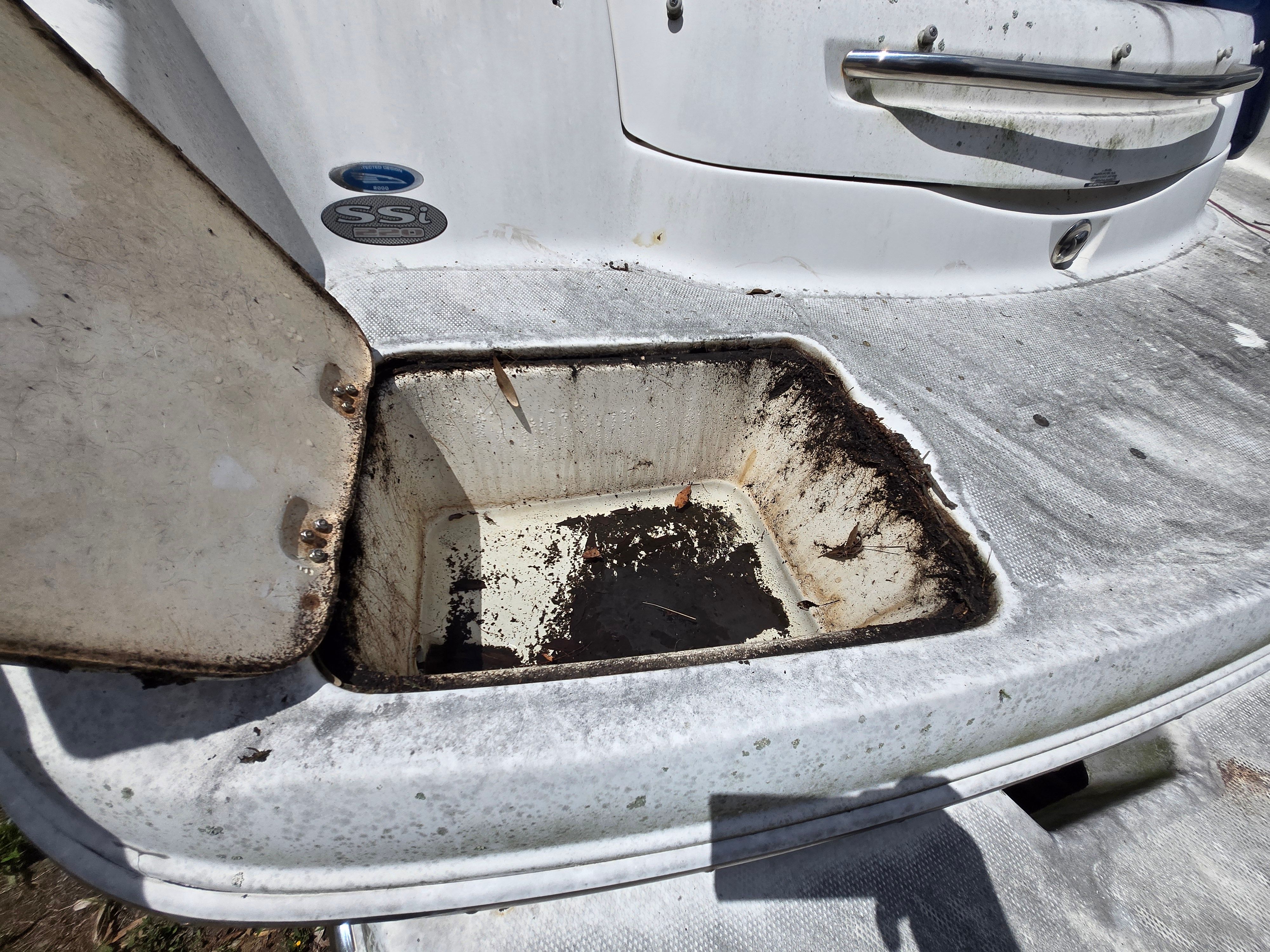 An open storage compartment on a 2006 Chaparral 220 SSi boat, with some dirt inside.