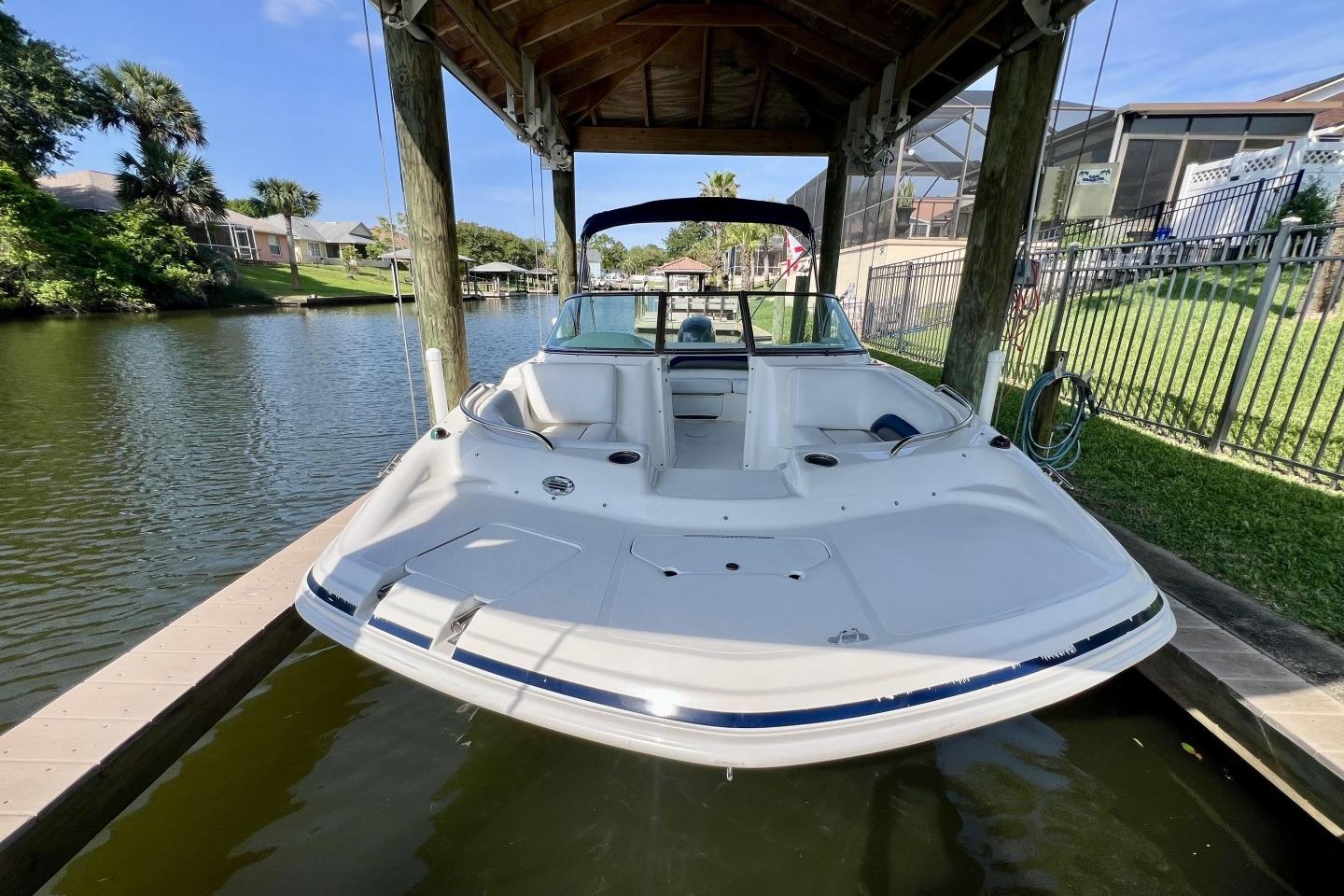 2013 Hurricane SunDeck 187 OB boat docked under a wooden canopy on a calm river.