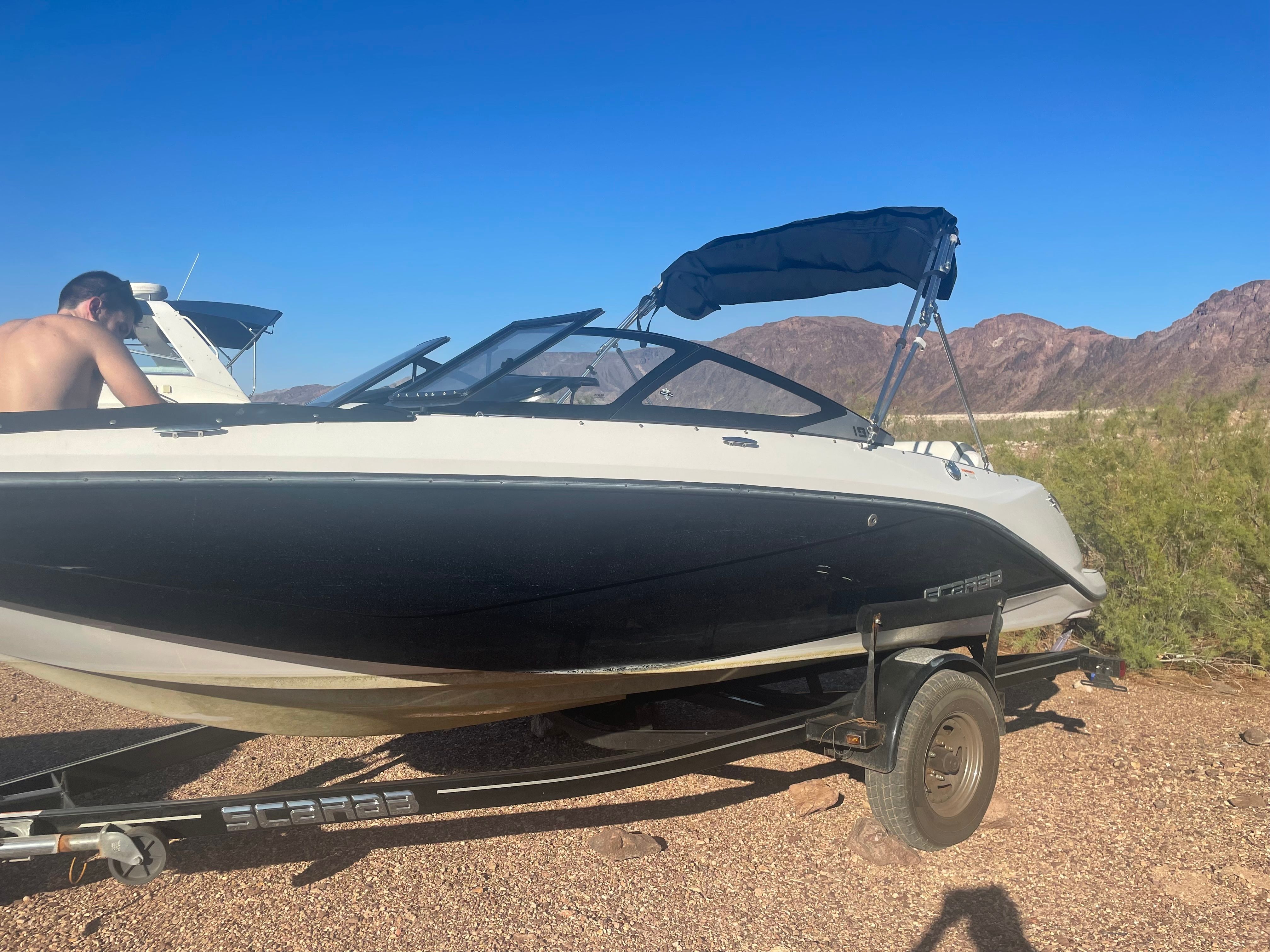 A 2019 Scarab 195 G boat on a trailer in a dry, mountainous landscape.