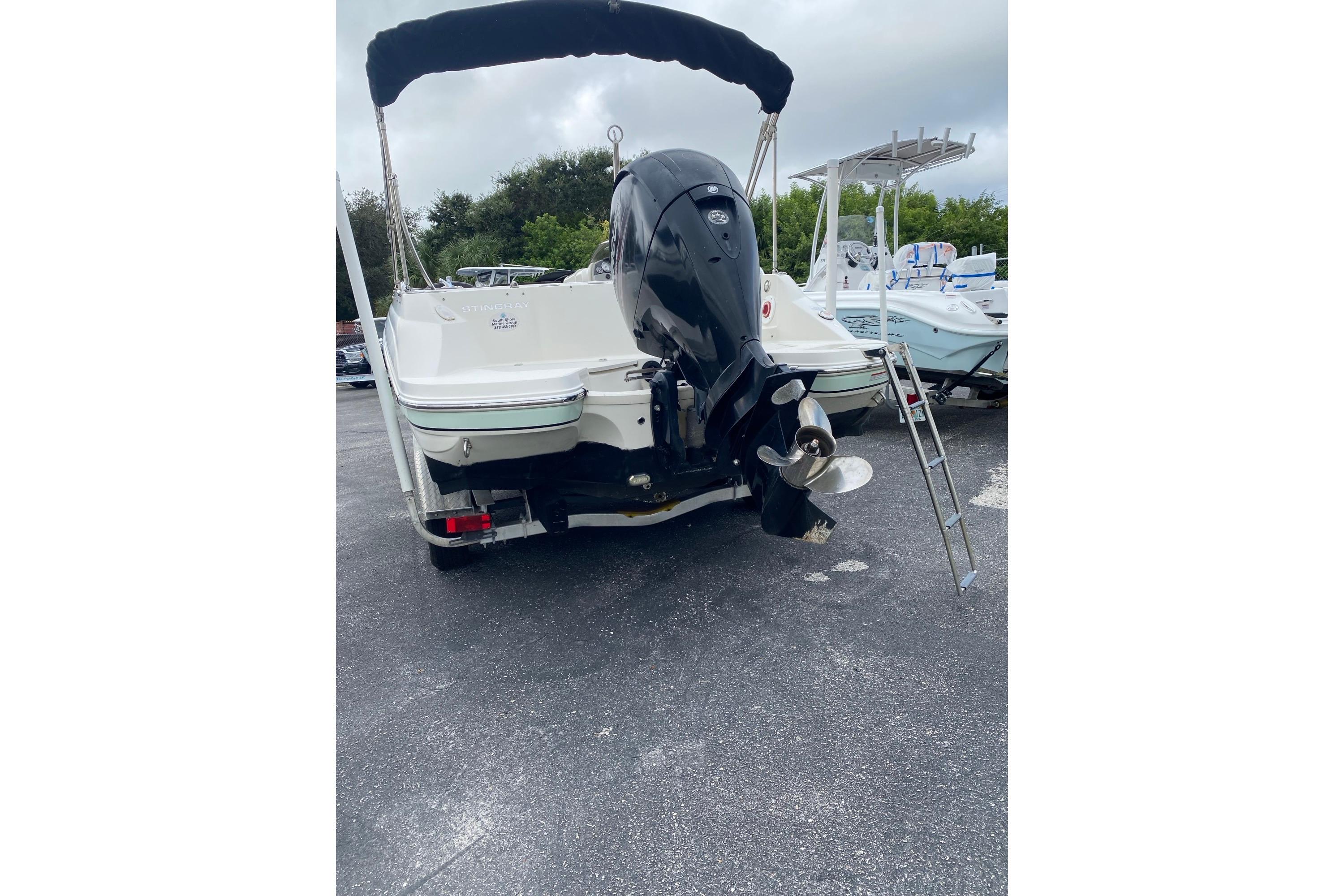 2018 Stingray 212 SC boat with outboard motor and ladder, parked on asphalt.