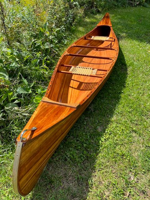 A handcrafted cedar strip canoe rests on a grassy lawn.