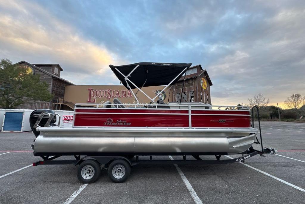 2026 Sun Tracker Fishin' Barge 22 DLX pontoon boat on trailer, parked outdoors.