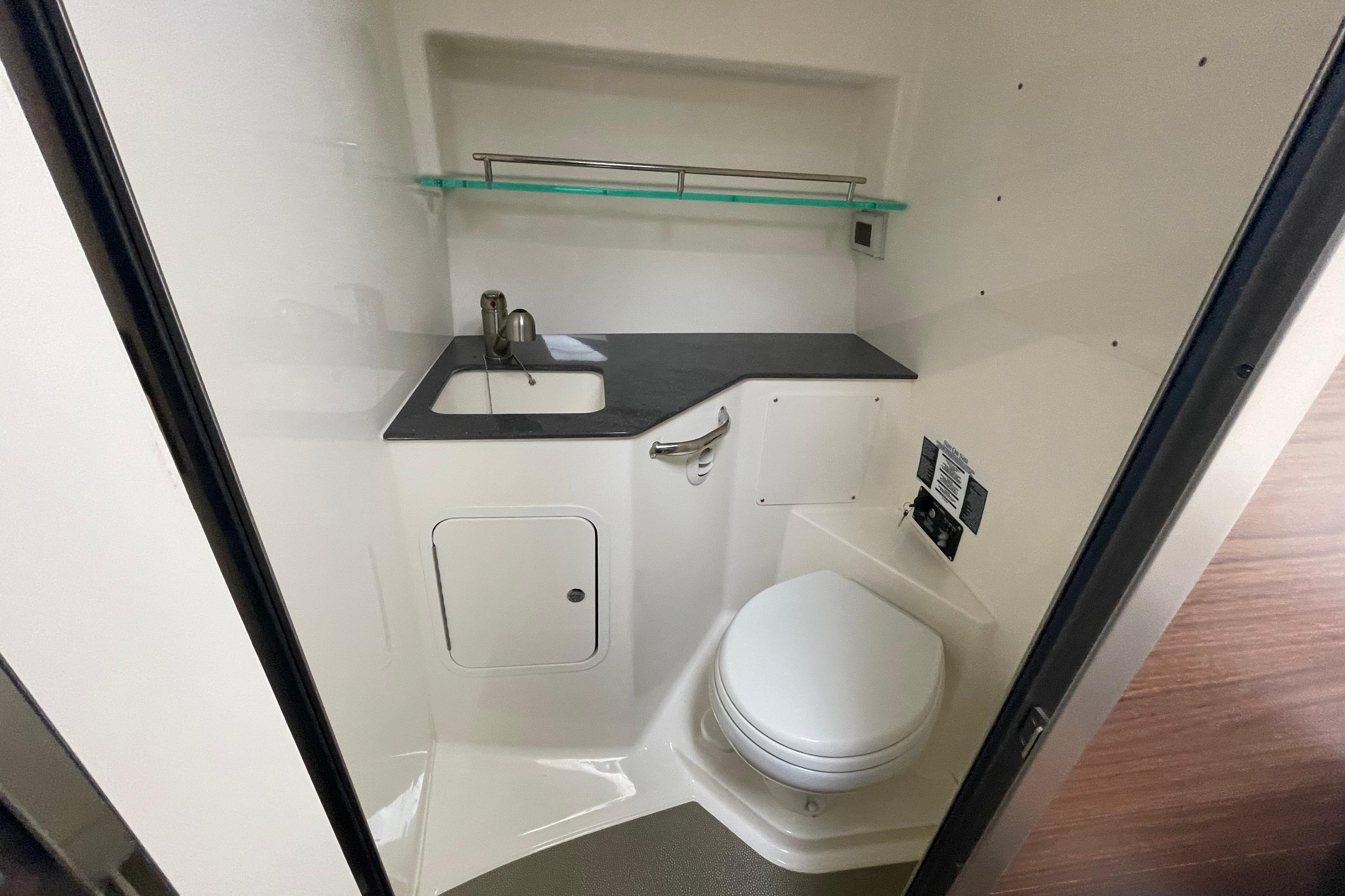 2023 Boston Whaler 325 Conquest bathroom with sink, toilet, and storage shelf.