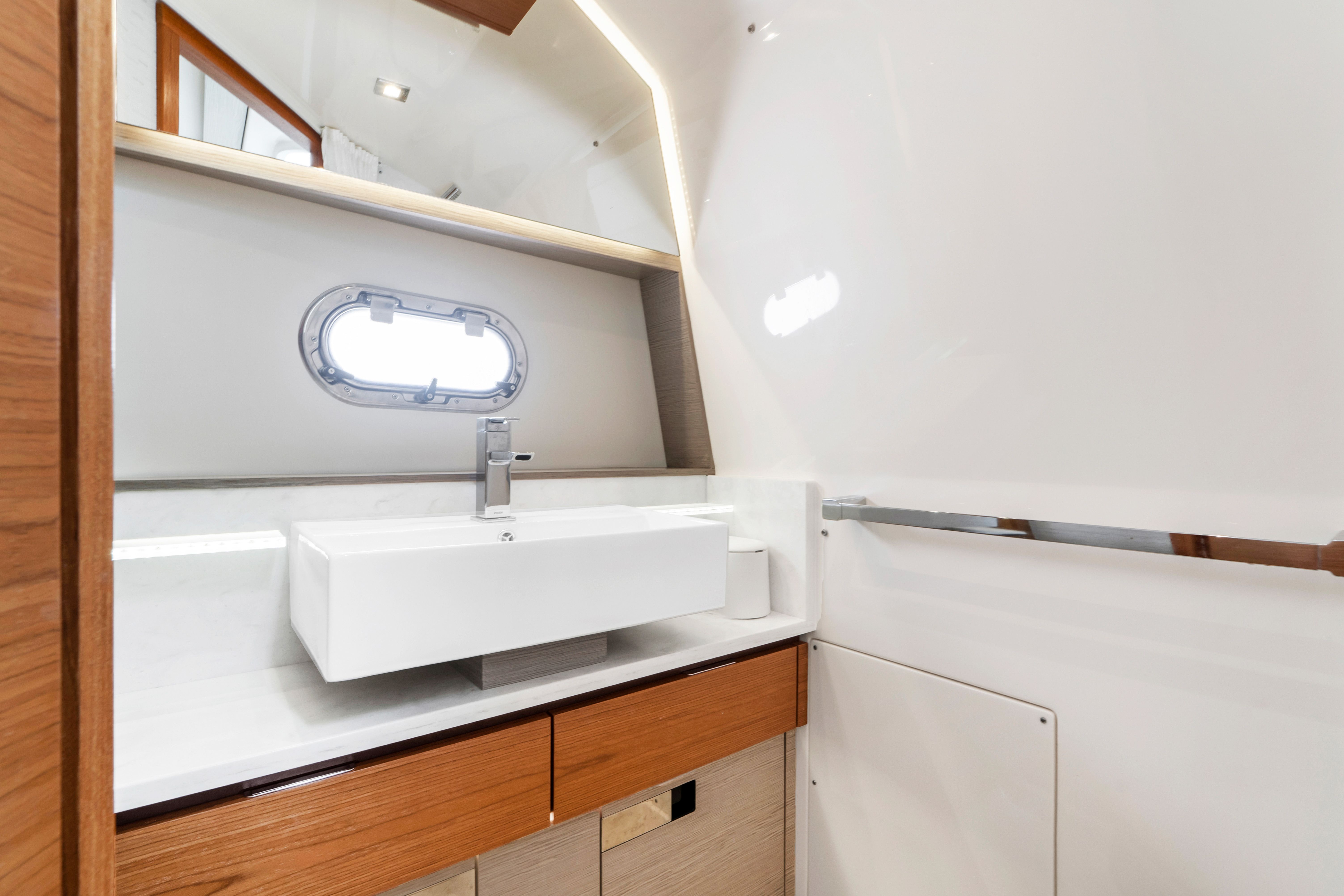 Modern yacht bathroom with sink, wooden cabinets, and a porthole.