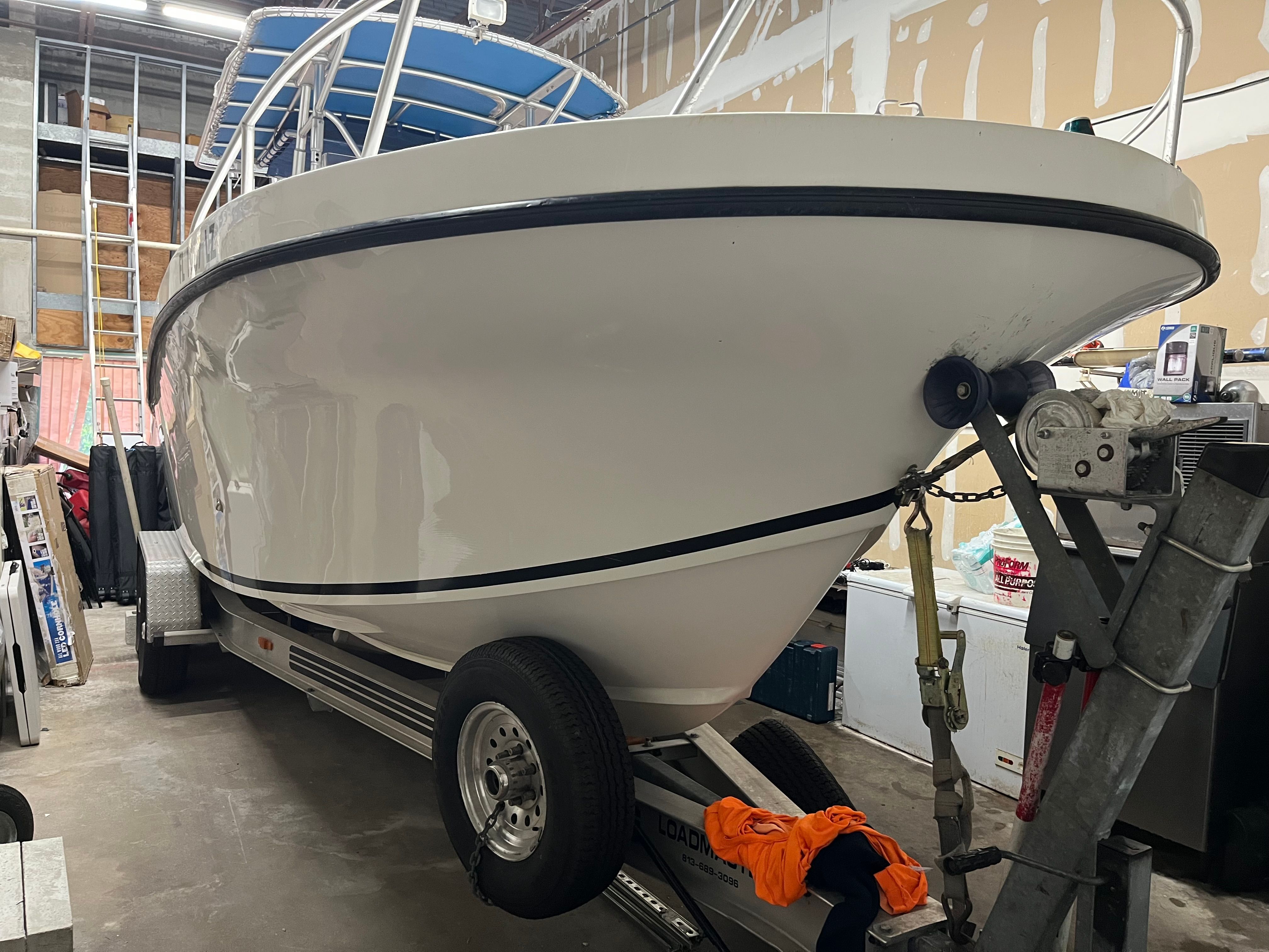A white boat on a trailer in a garage. It features a blue canopy.