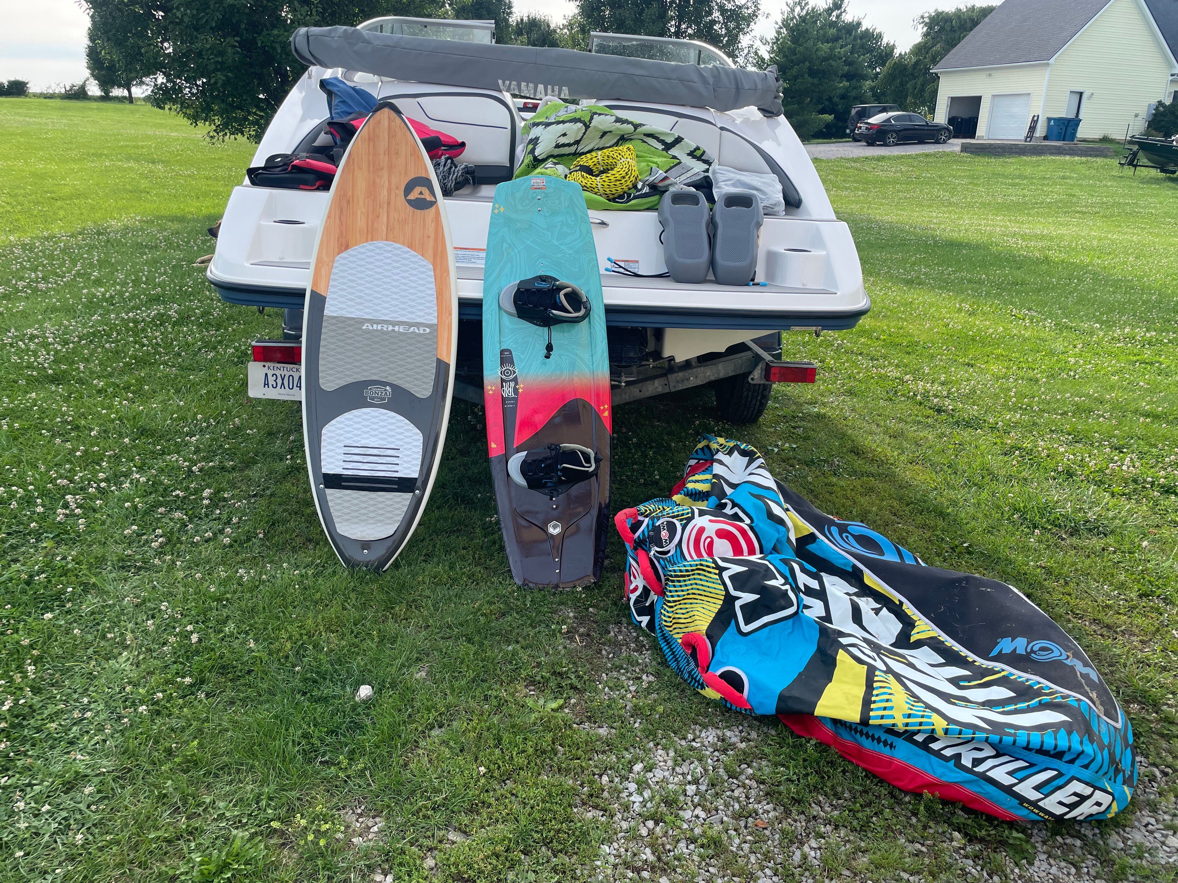 A 2019 Yamaha SX210 boat on grass with two surfboards and an inflatable tube beside it.
