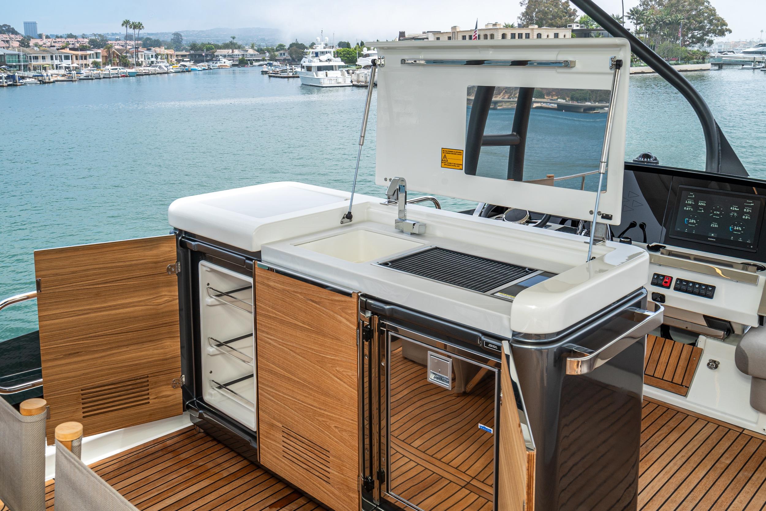 Outdoor kitchen on 2024 Prestige X60 yacht with grill and storage, overlooking marina.