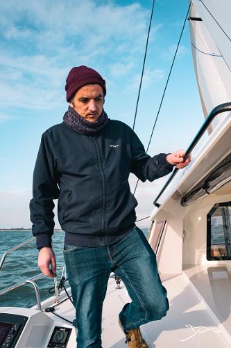 Man on Nautitech 40 Open 2025 sailboat, wearing a beanie and jacket, under clear blue sky.