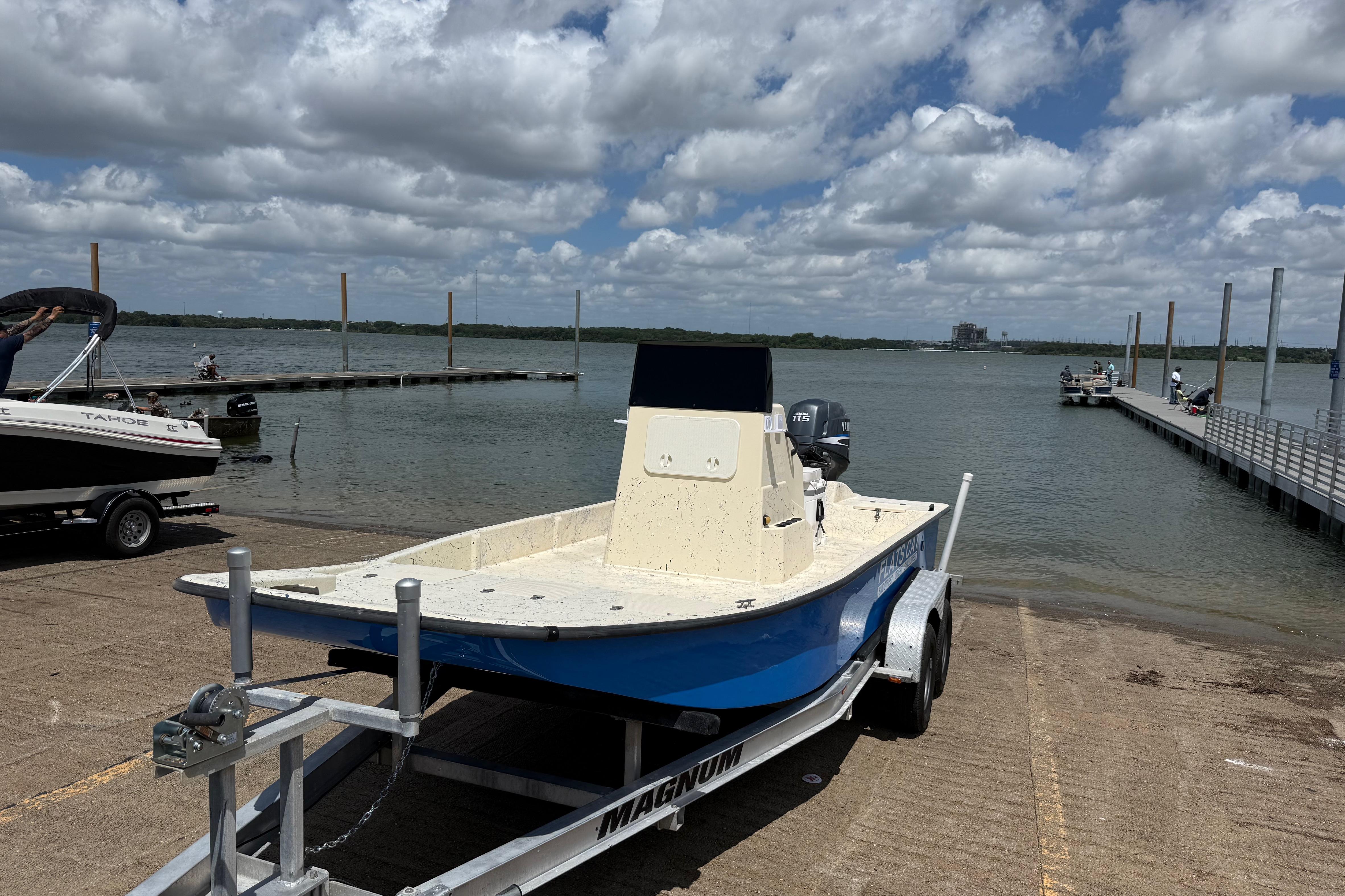 2007 Flats Cat 19 boat on trailer by lake under cloudy sky.