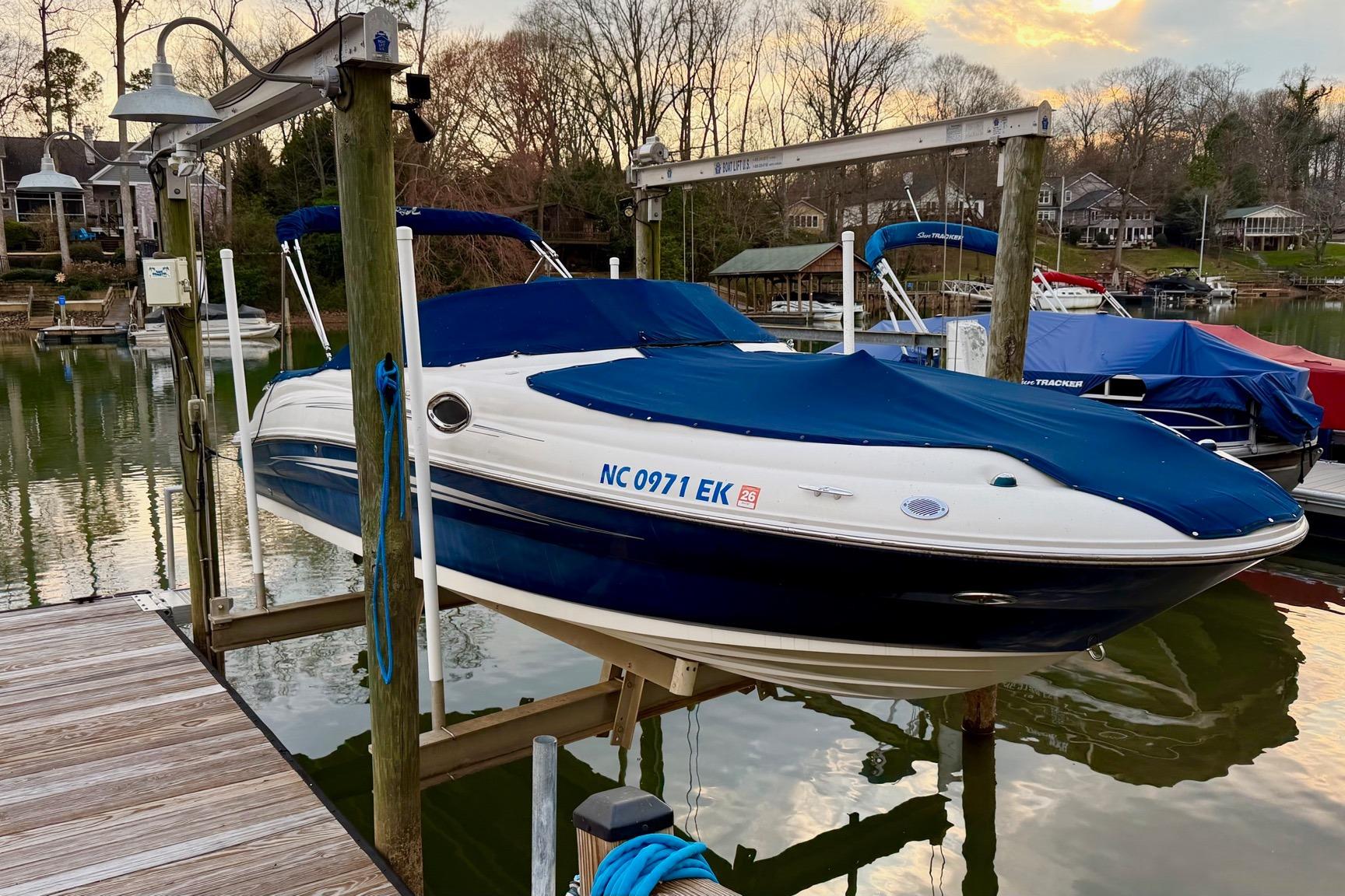 2008 Sea Ray 240 Sundeck boat docked with blue cover at a serene lakeside.