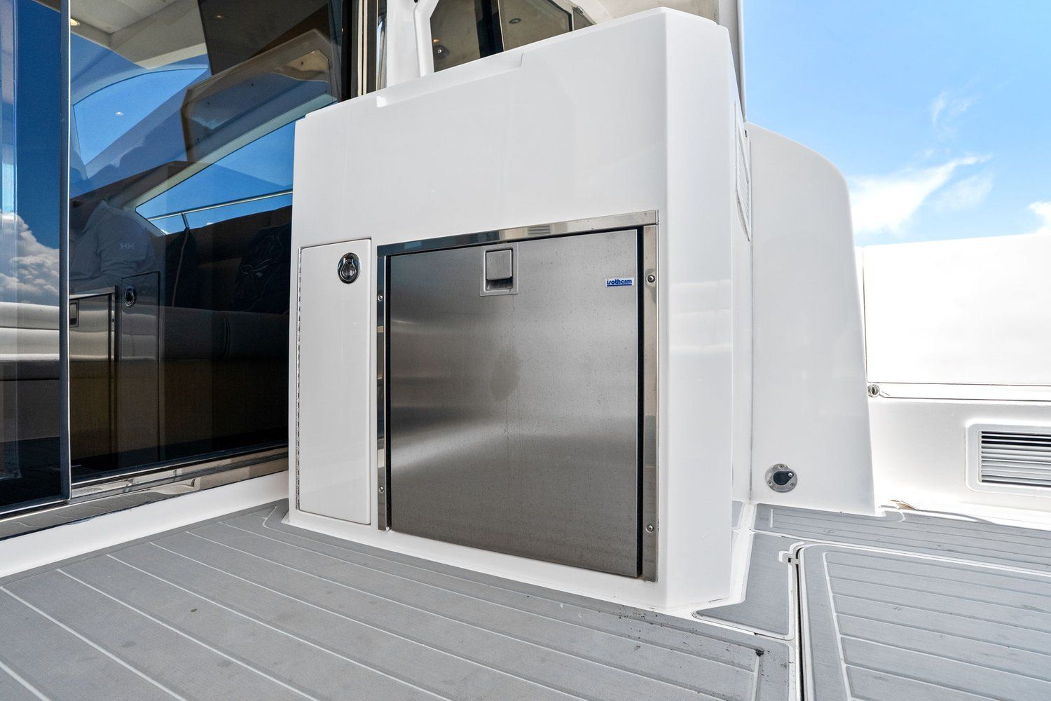 A modern catamaran with a stainless steel refrigerator on deck, surrounded by white surfaces.