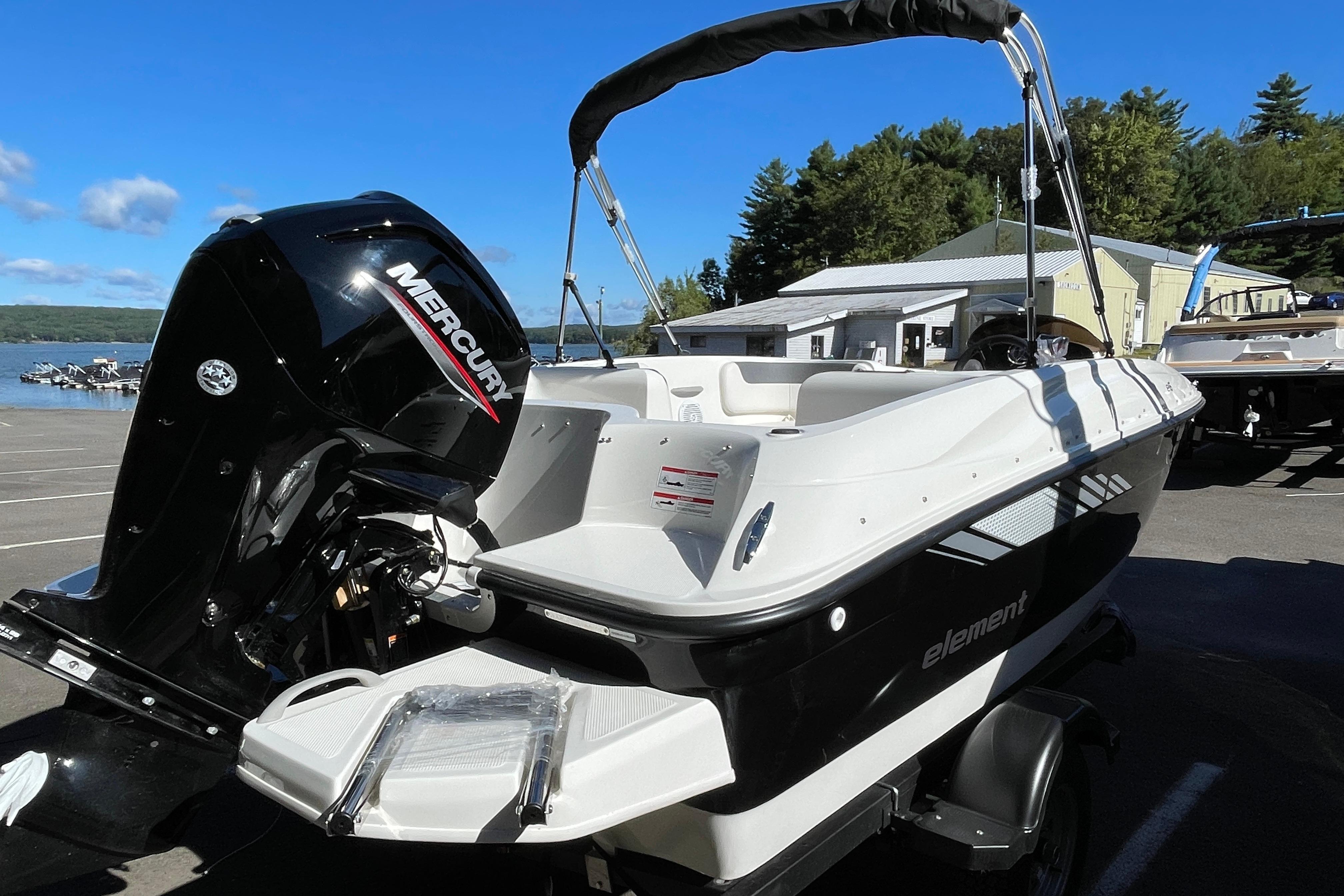 2026 Bayliner Element E16 boat with Mercury engine, parked near a lake under clear blue sky.