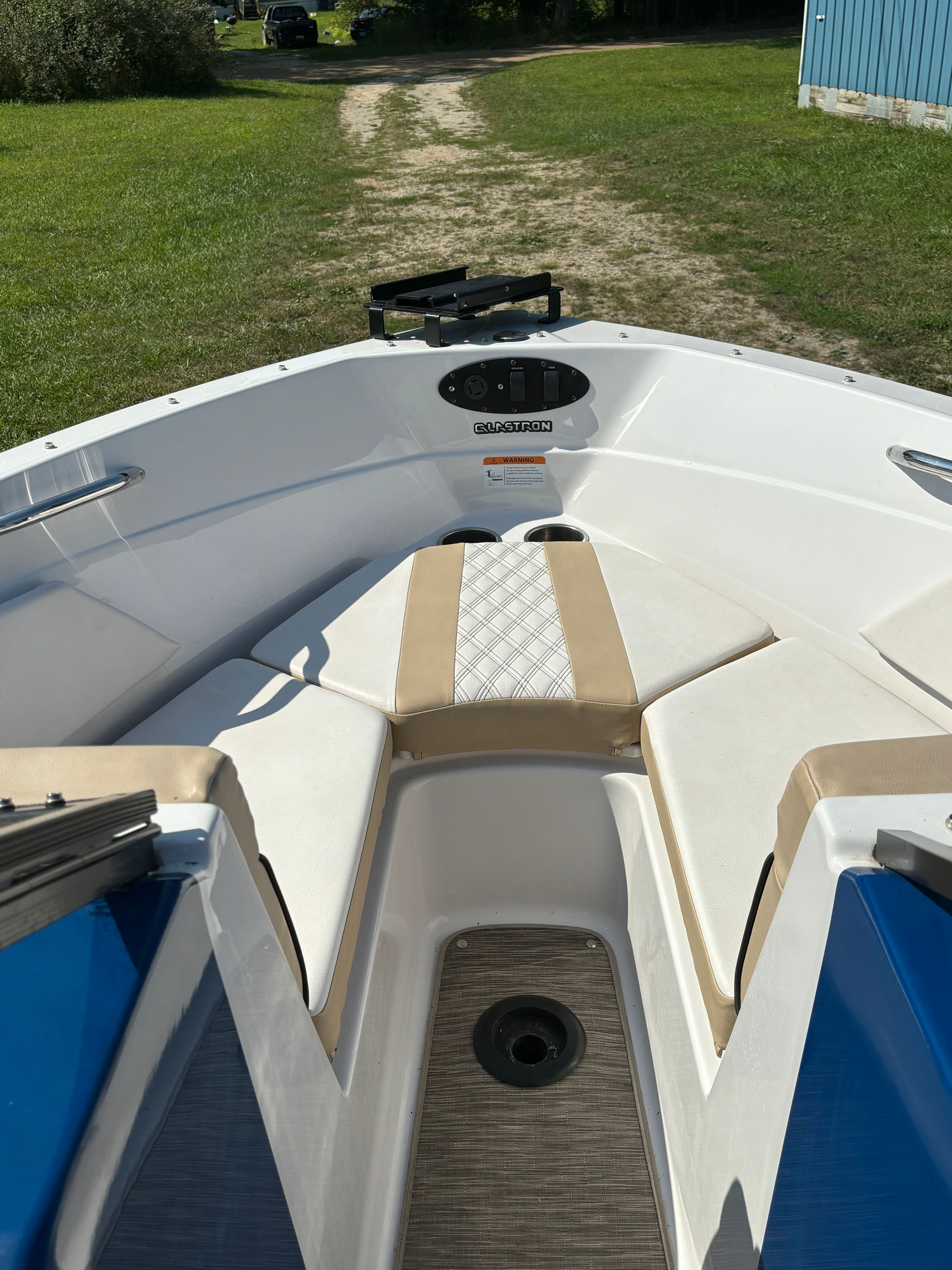 The boat has white and beige seats with blue accents, on a grassy path.