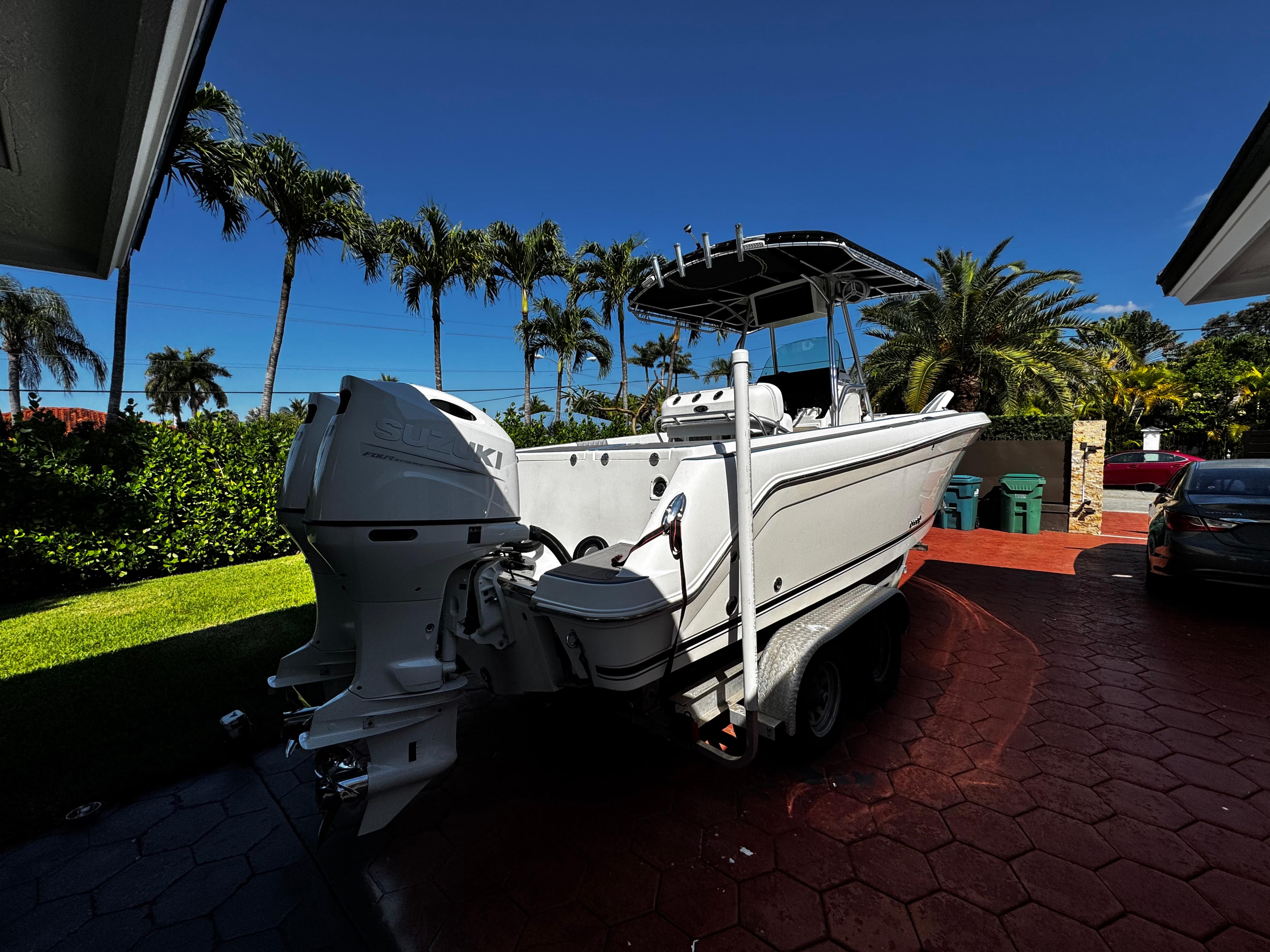 2004 Robalo R 260 boat on trailer, parked in a tropical driveway.