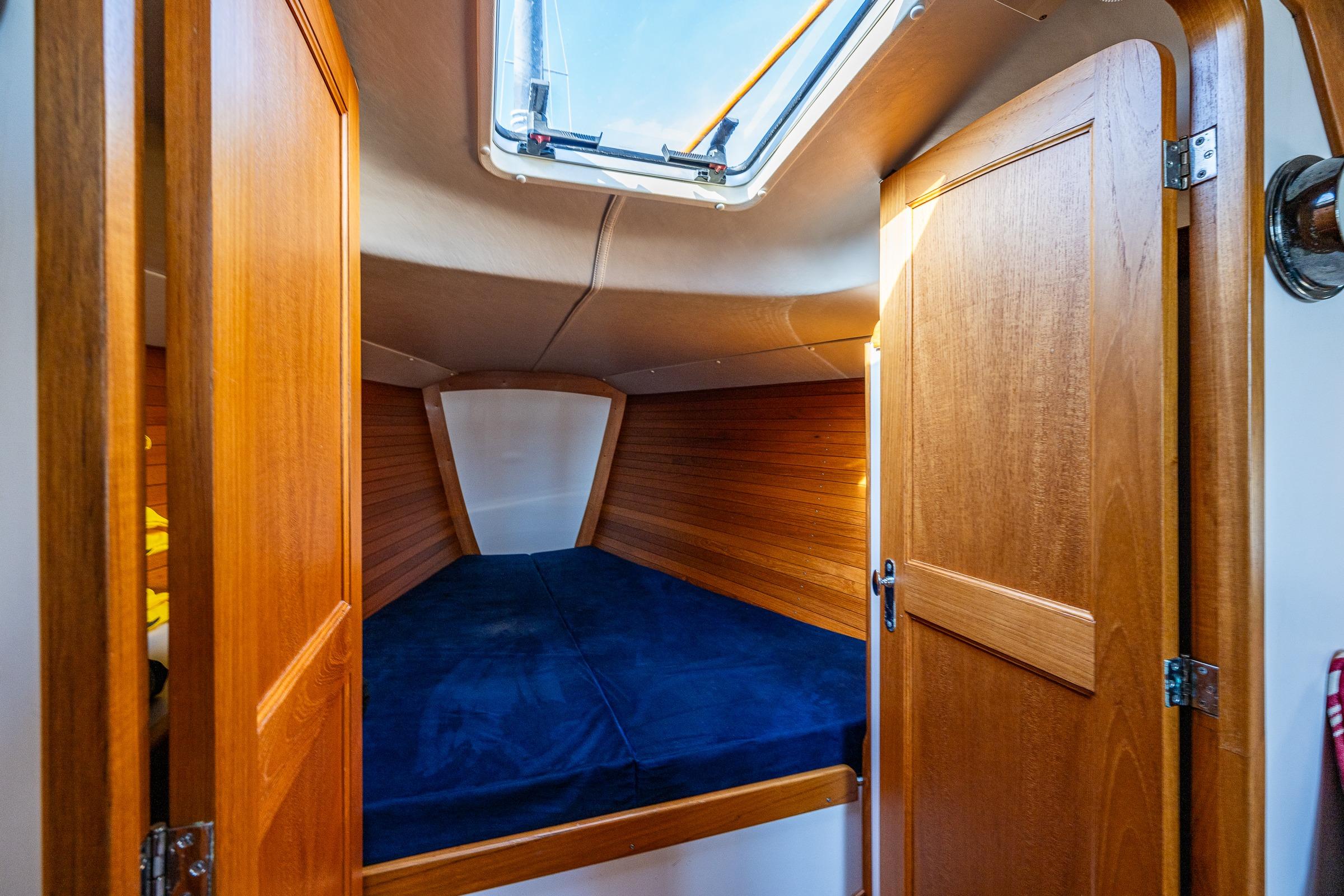 Cozy cabin interior of 2007 J Boats J/124 with wooden finish and blue bedding.