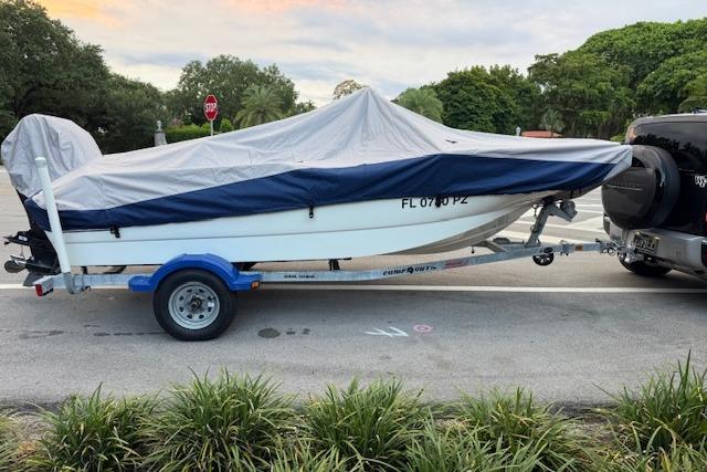 Covered 2016 Boston Whaler 150 Montauk on trailer, parked beside a vehicle.