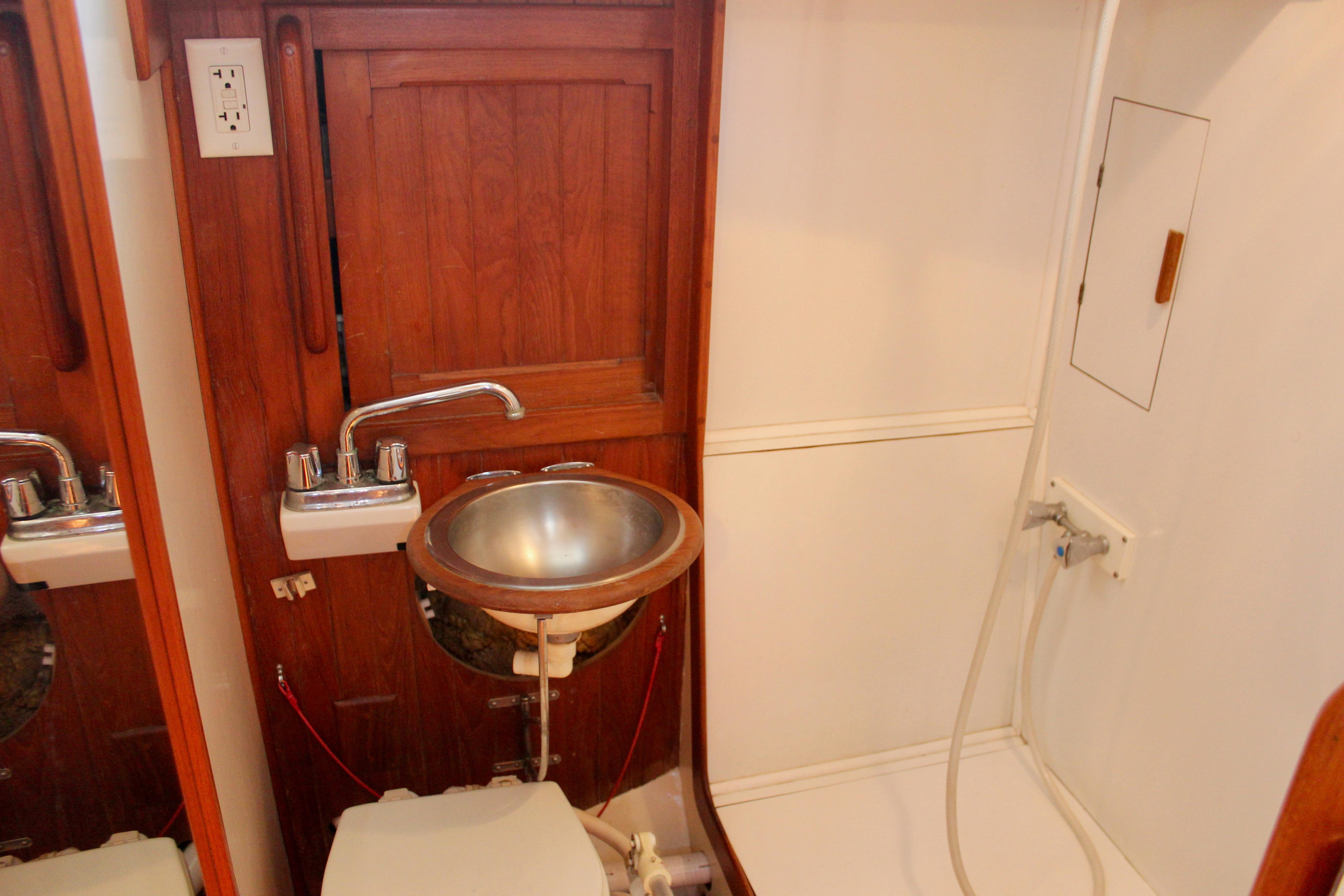 1981 Kelly Peterson 46 yacht bathroom with wooden cabinetry, stainless steel sink, and shower area.