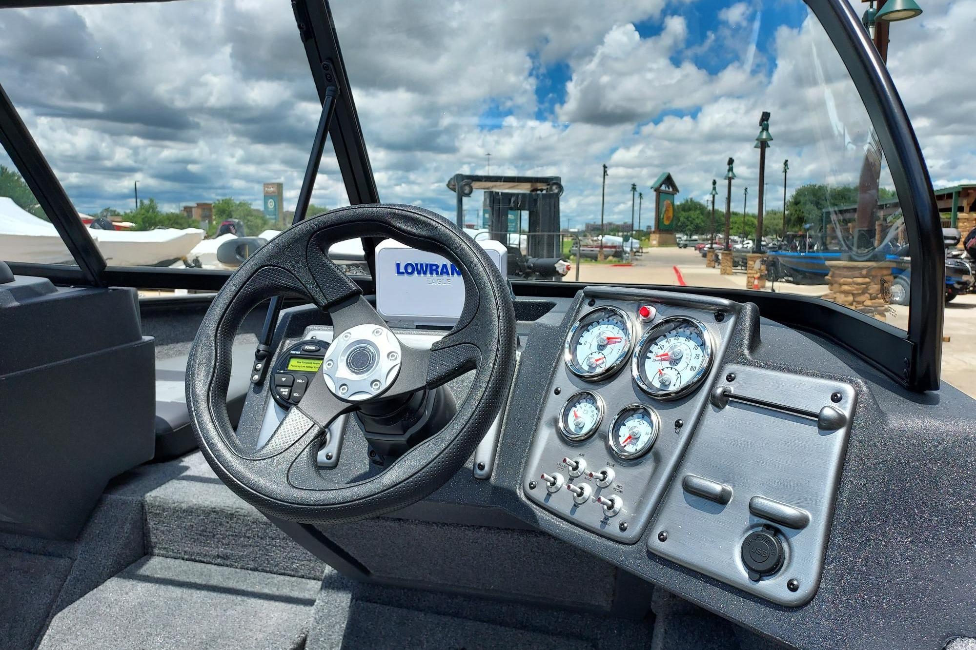 2026 Tracker Pro Guide V-175 Combo boat dashboard with steering wheel and gauges under a cloudy sky.