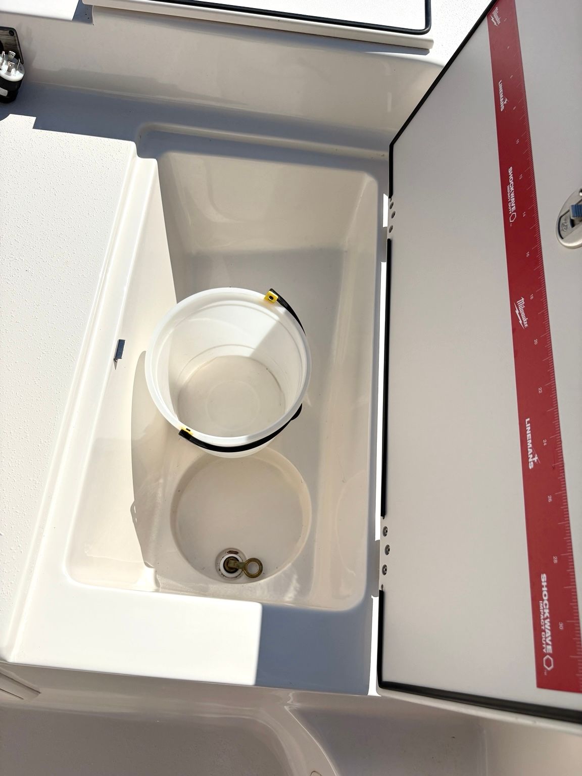 An open storage compartment on a boat with a bucket and some coins inside.